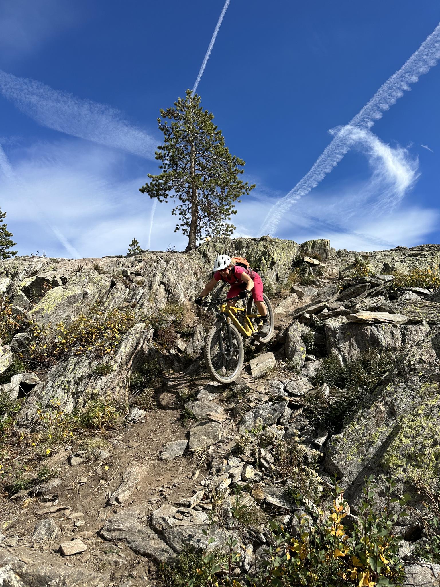 Mountain biker navigates a steep, rocky descent under a blue sky.