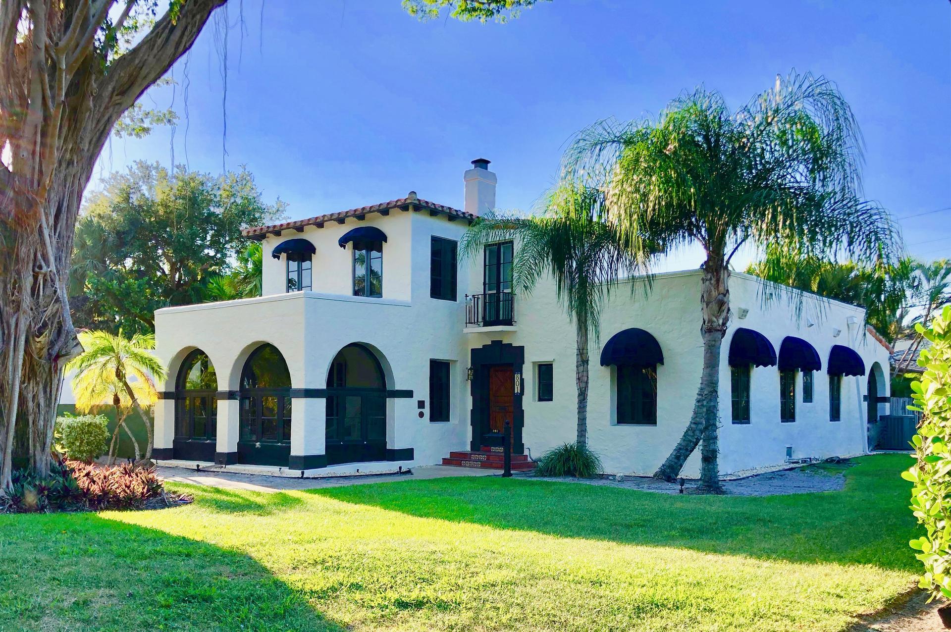 A large white house with dark accents and green lawn under a sunny sky.