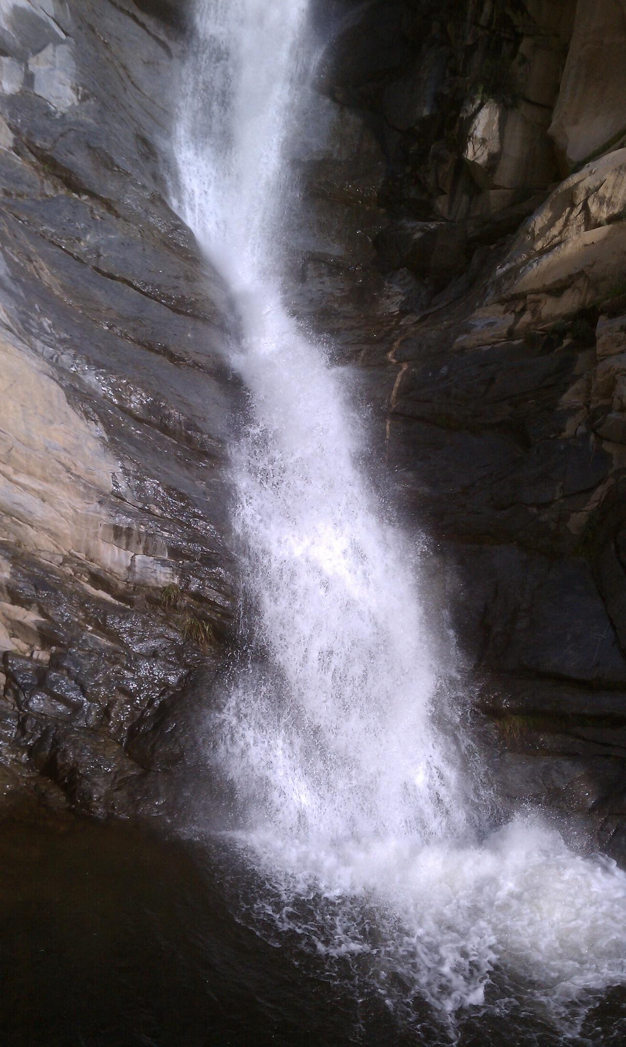 A powerful waterfall cascades down a dark, rocky cliff face.