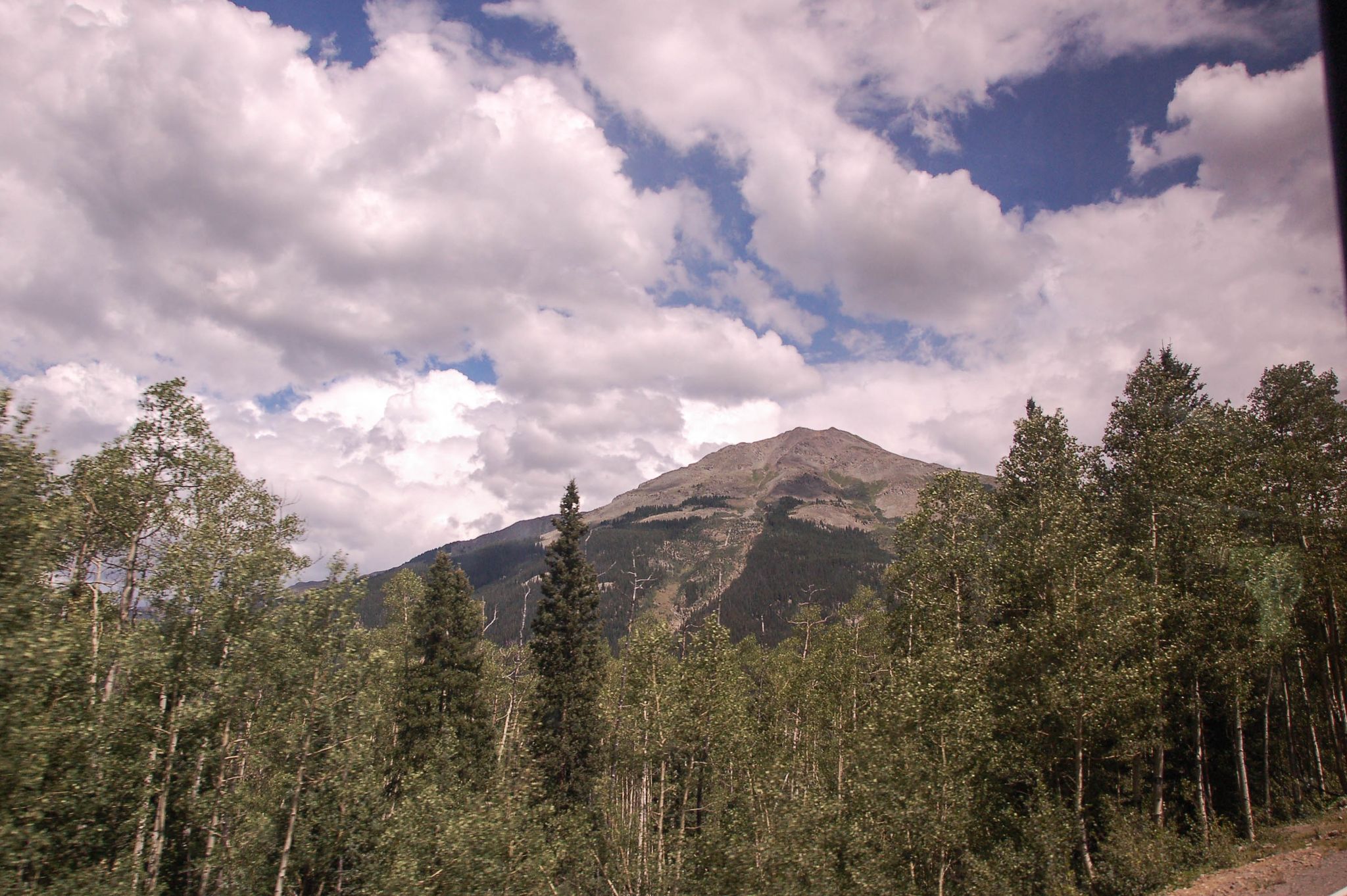 A mountain peak rises above a dense forest under a cloudy sky. - Kendall Mountain Road
