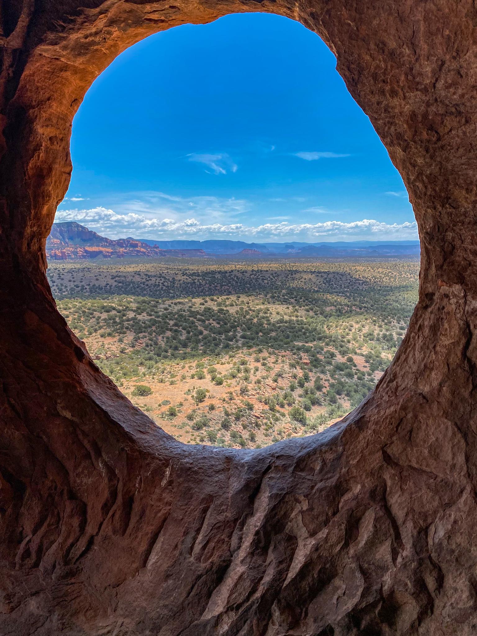 Bright blue sky and arid landscape viewed through a dark cave opening.