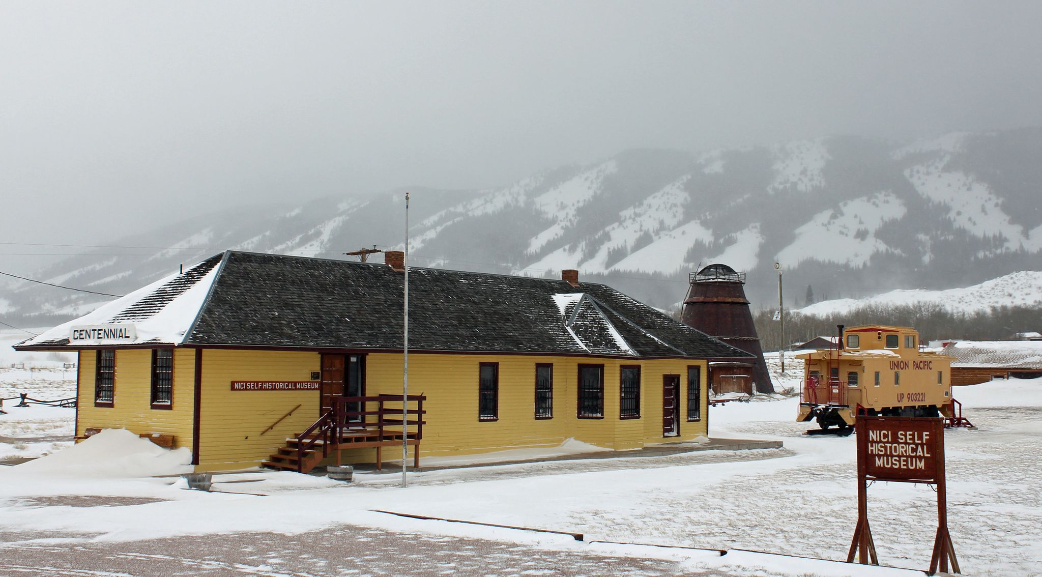 Yellow building in snowy landscape with distant mountains under an overcast sky. - Snowy Range Road (Centennial, Wyoming to North Platte River)
