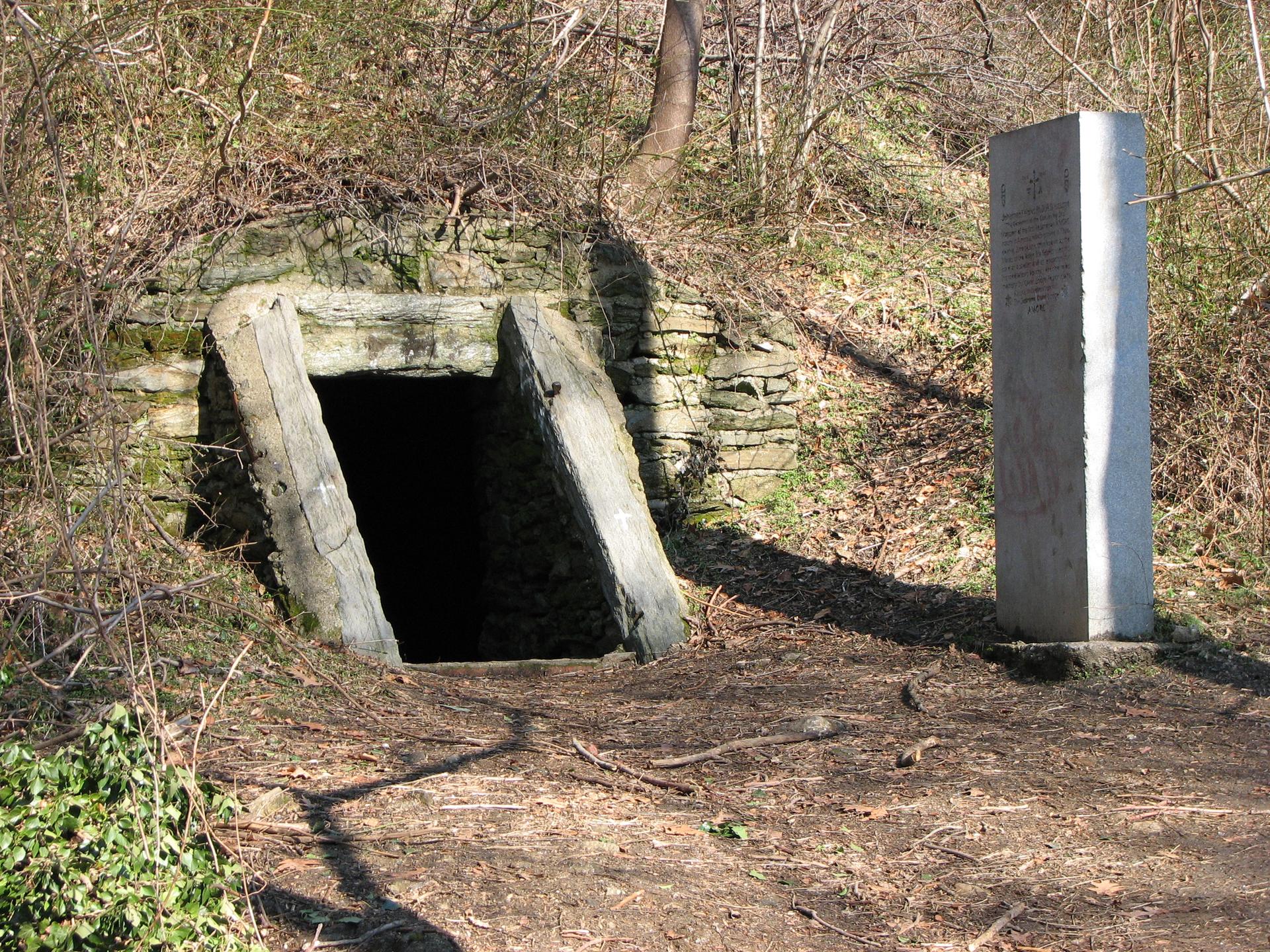A dark mine entrance in a hillside next to a tall stone monument.