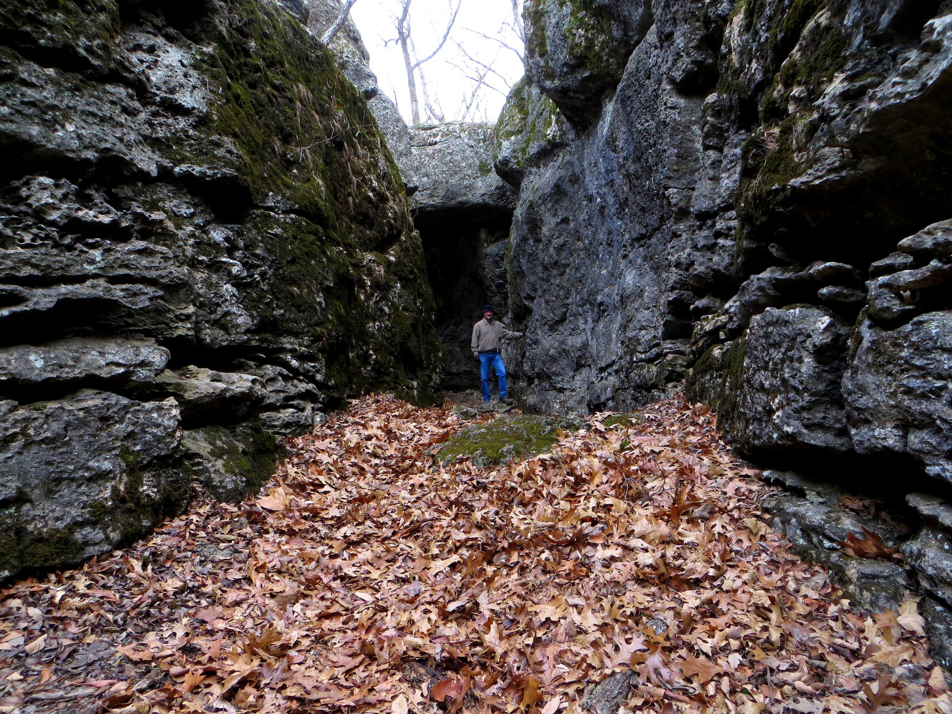 Person standing in a deep, narrow rock crevice filled with leaves.