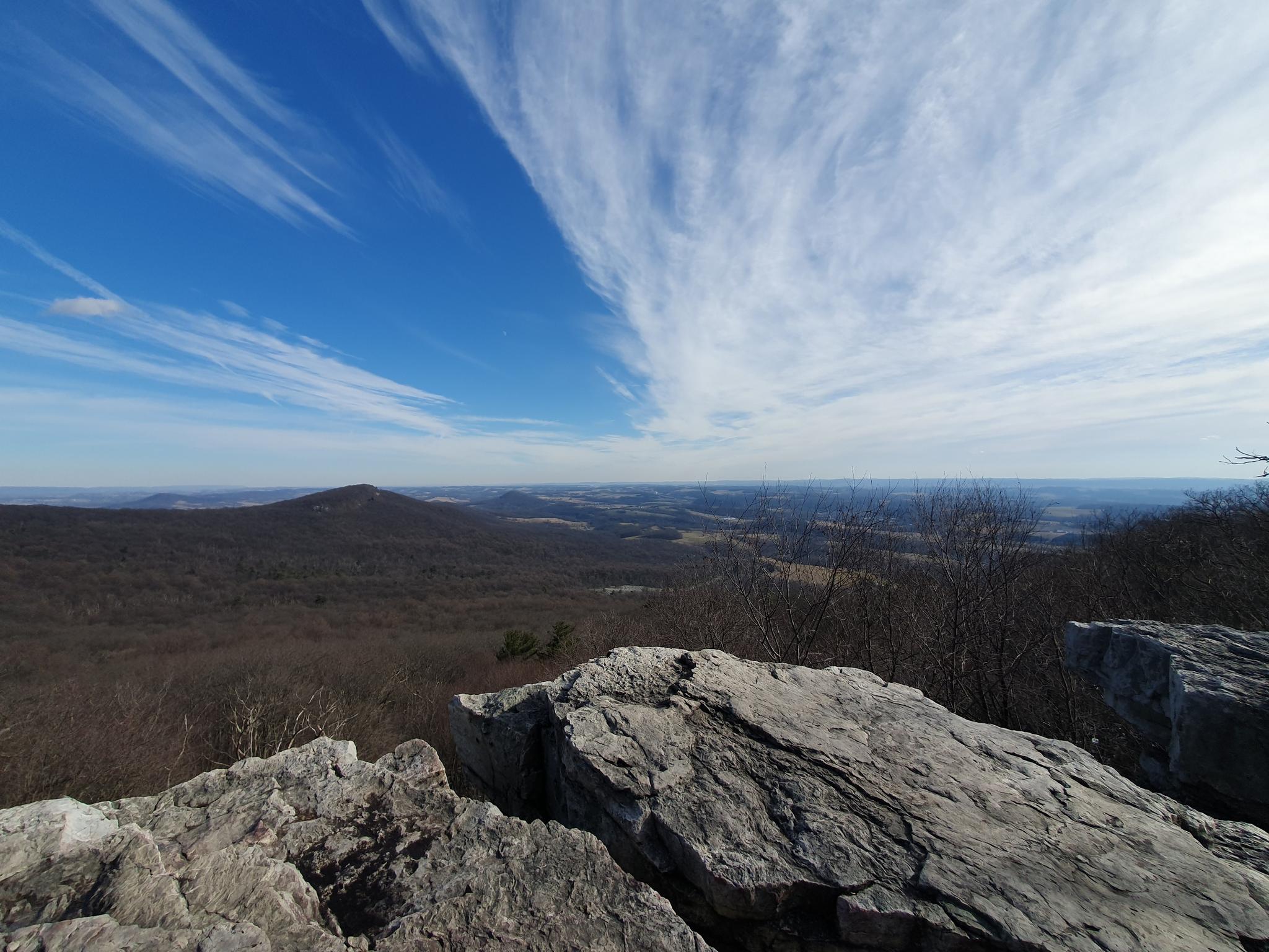 Panoramic view from a rocky cliff over a vast forested landscape. Bright sky.