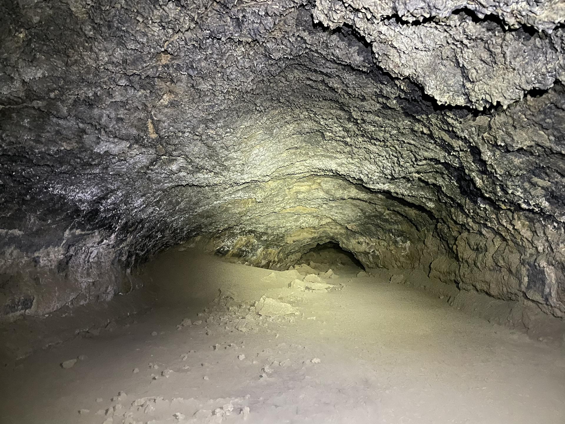 Dark cave interior with rough, textured rock walls illuminated by a spotlight.