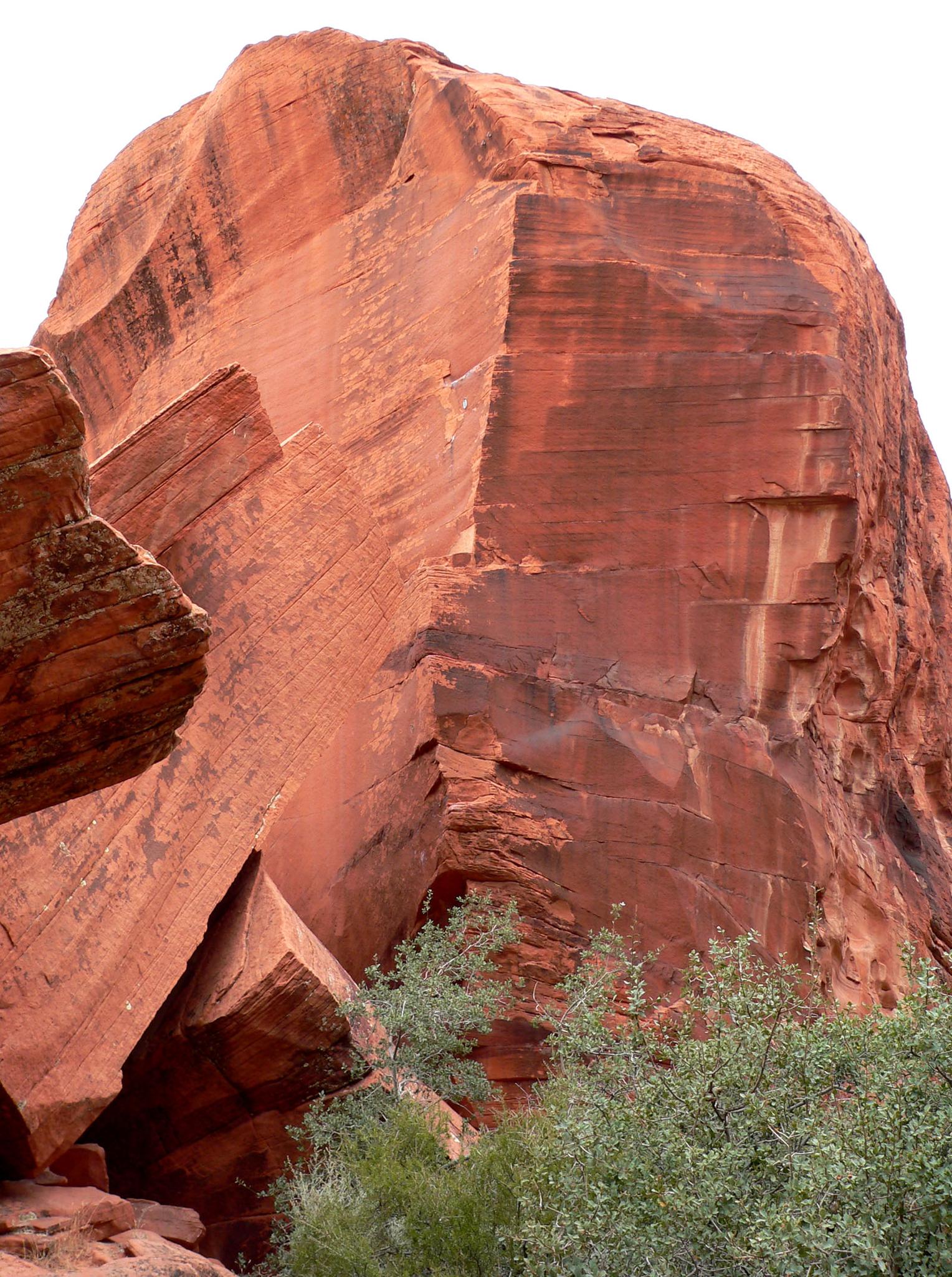 Close-up of a massive, textured red rock formation with green shrubs below.