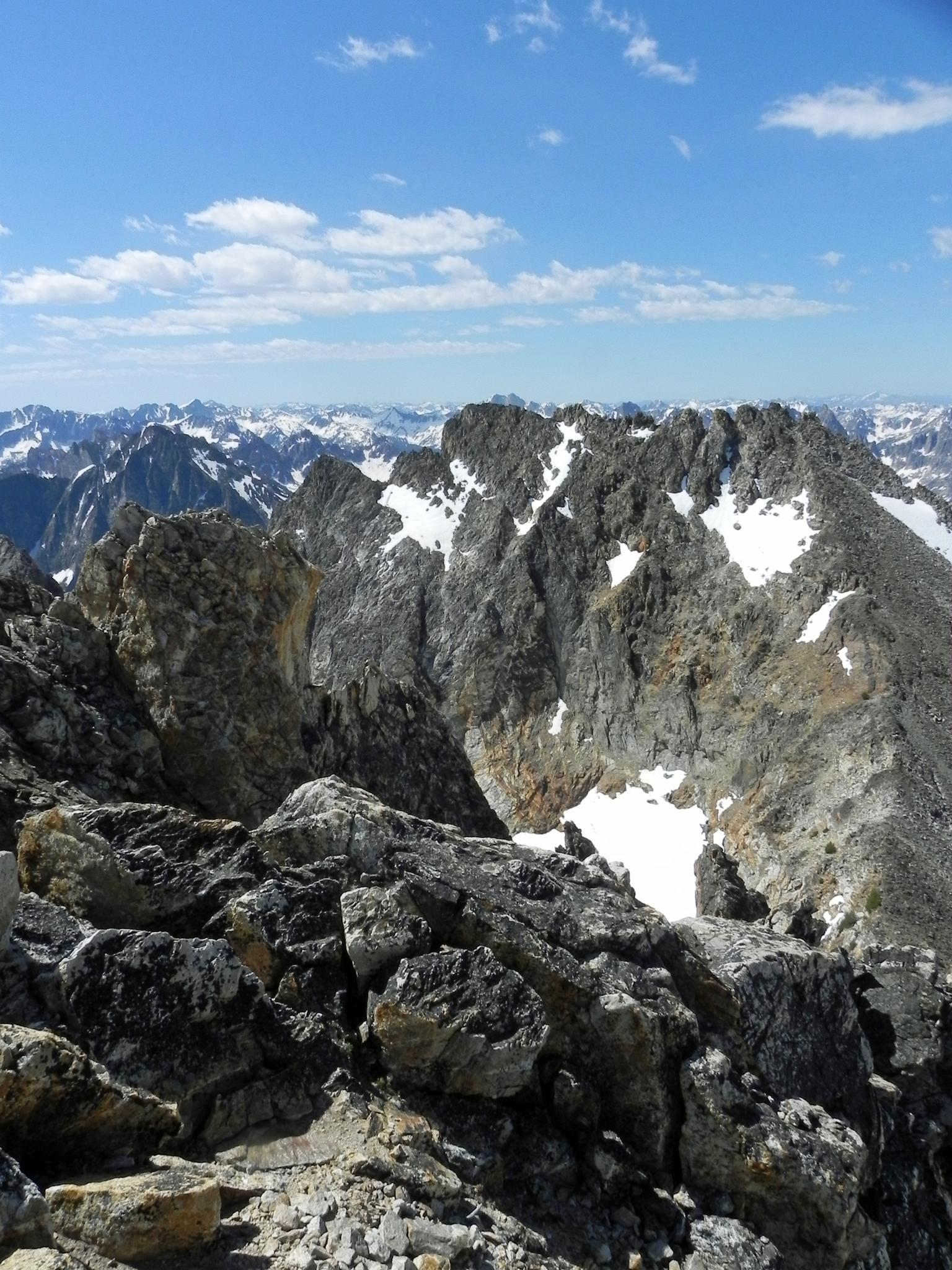 Rugged, snow-dusted mountain peaks under a bright blue sky with clouds.