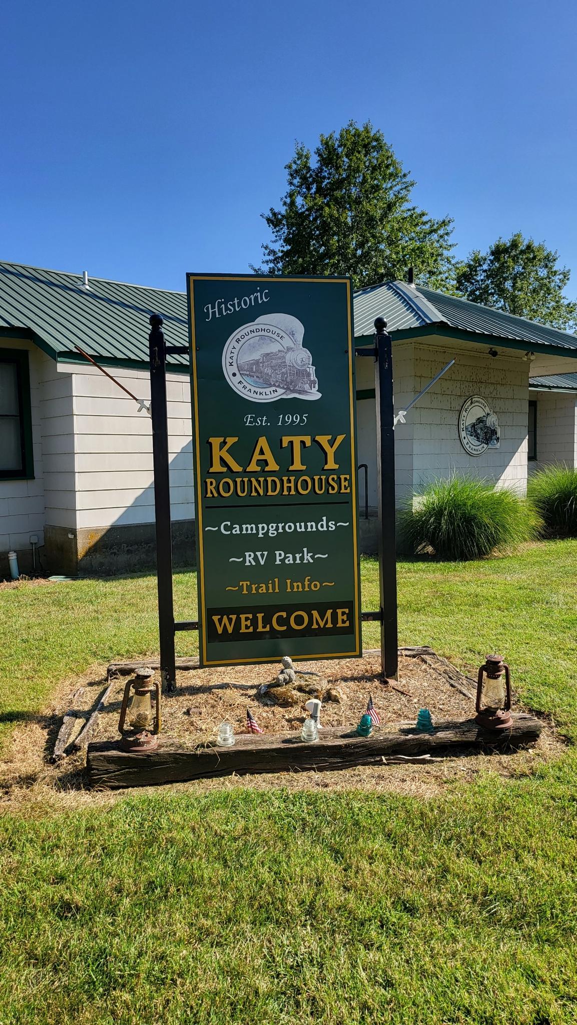 An outdoor sign for "Katy Roundhouse" in front of buildings on a sunny day.