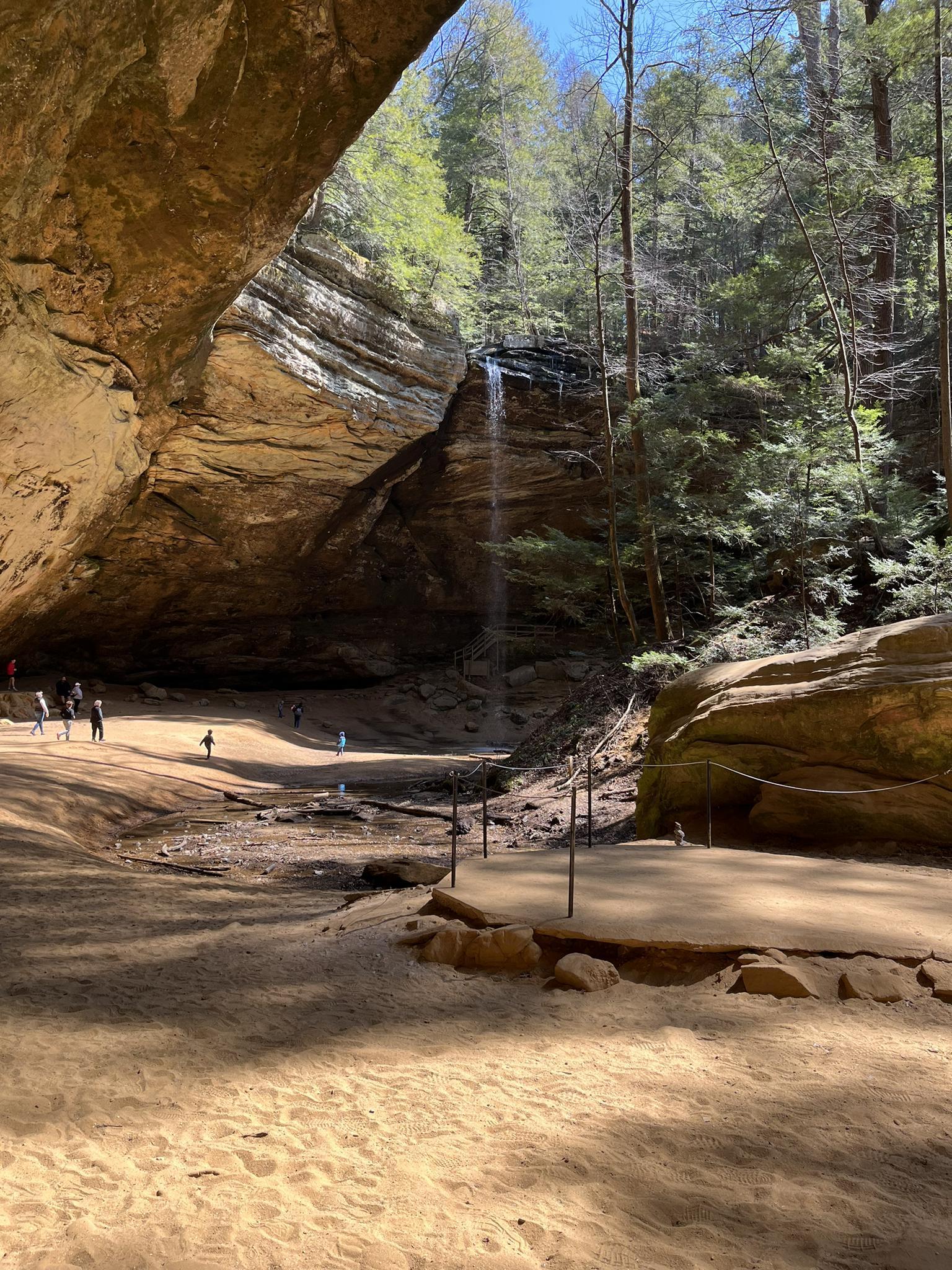 People exploring a large rock shelter with a small waterfall.