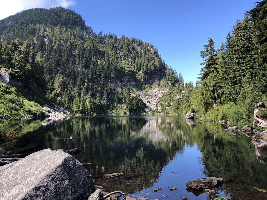 Serene mountain lake reflecting forested slopes under bright daylight.