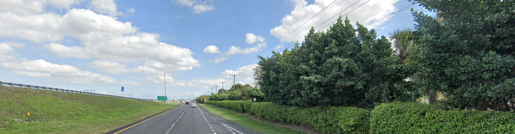 A wide highway with green embankments and dense trees under a cloudy sky.