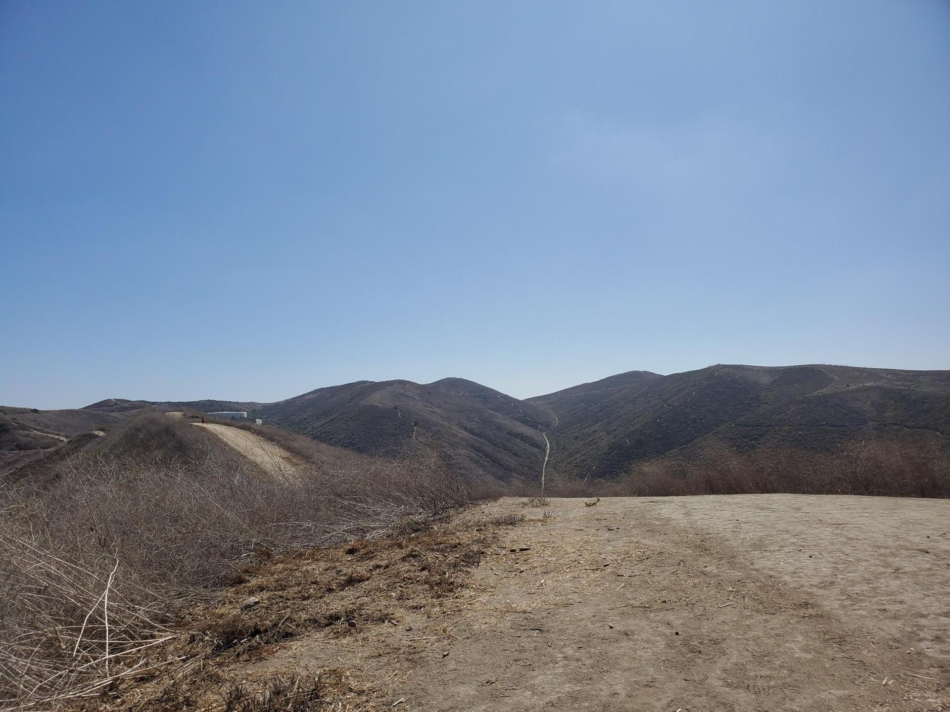 Expansive view of dry, rolling hills and mountains under a clear blue sky.