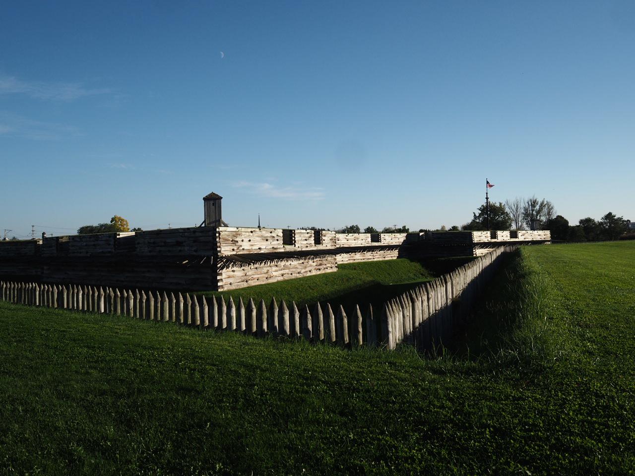 A wooden fort with a watchtower stands in a vast green field.