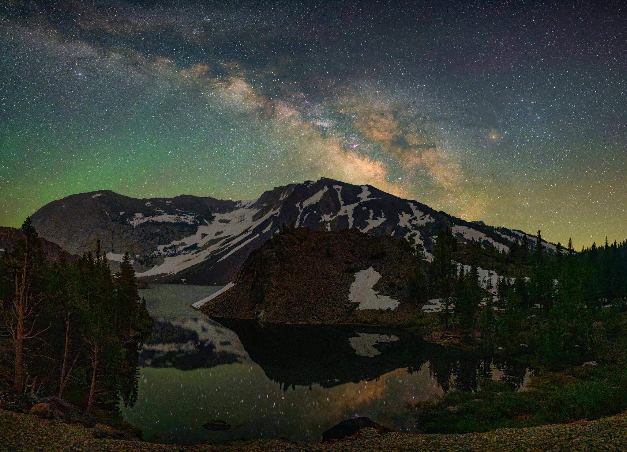 Mountain lake reflecting a starry sky with the Milky Way and green glow.