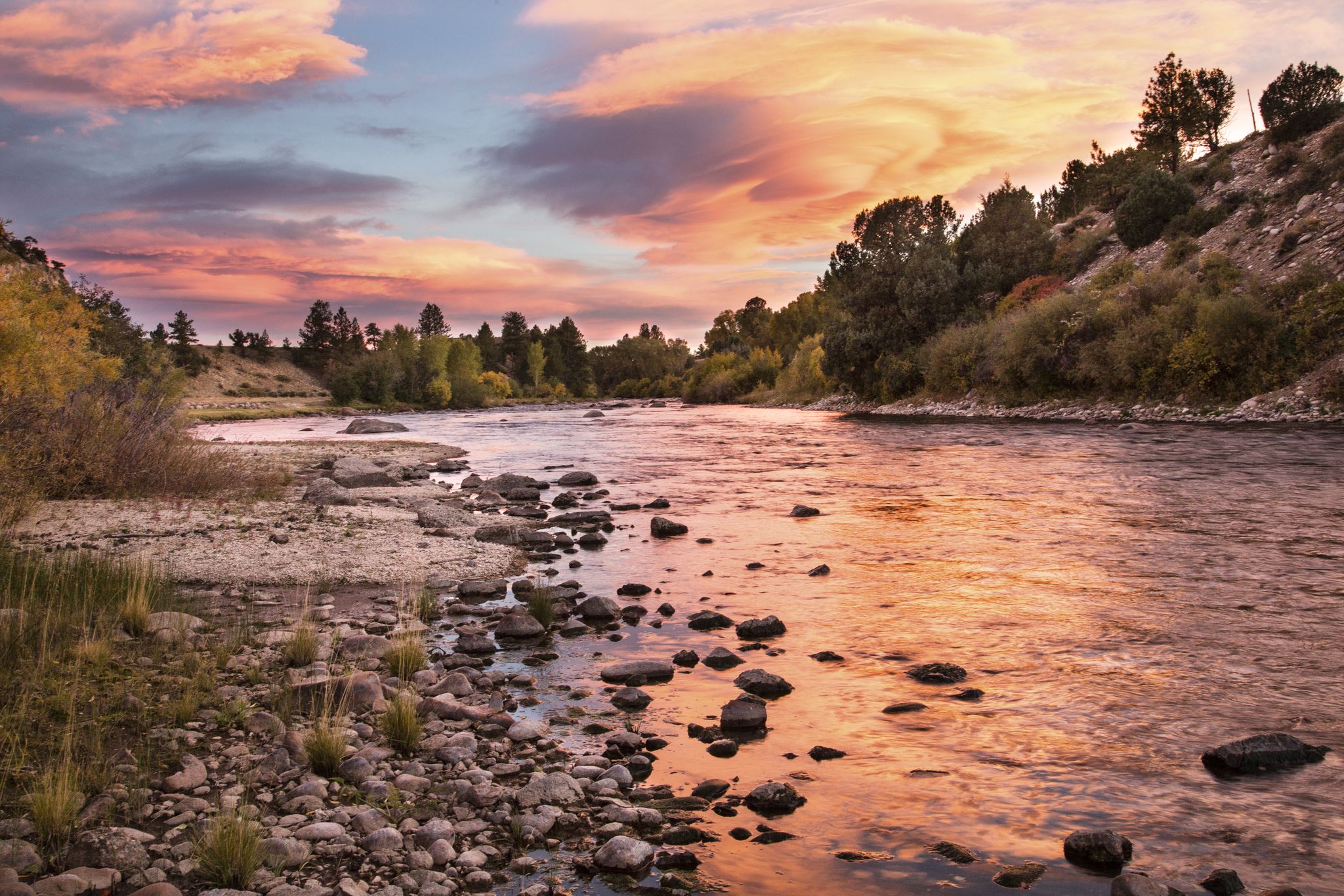 Scenic river with rocky banks and forested hills under a vibrant sunset. - Turret and River Bench Trail Loop