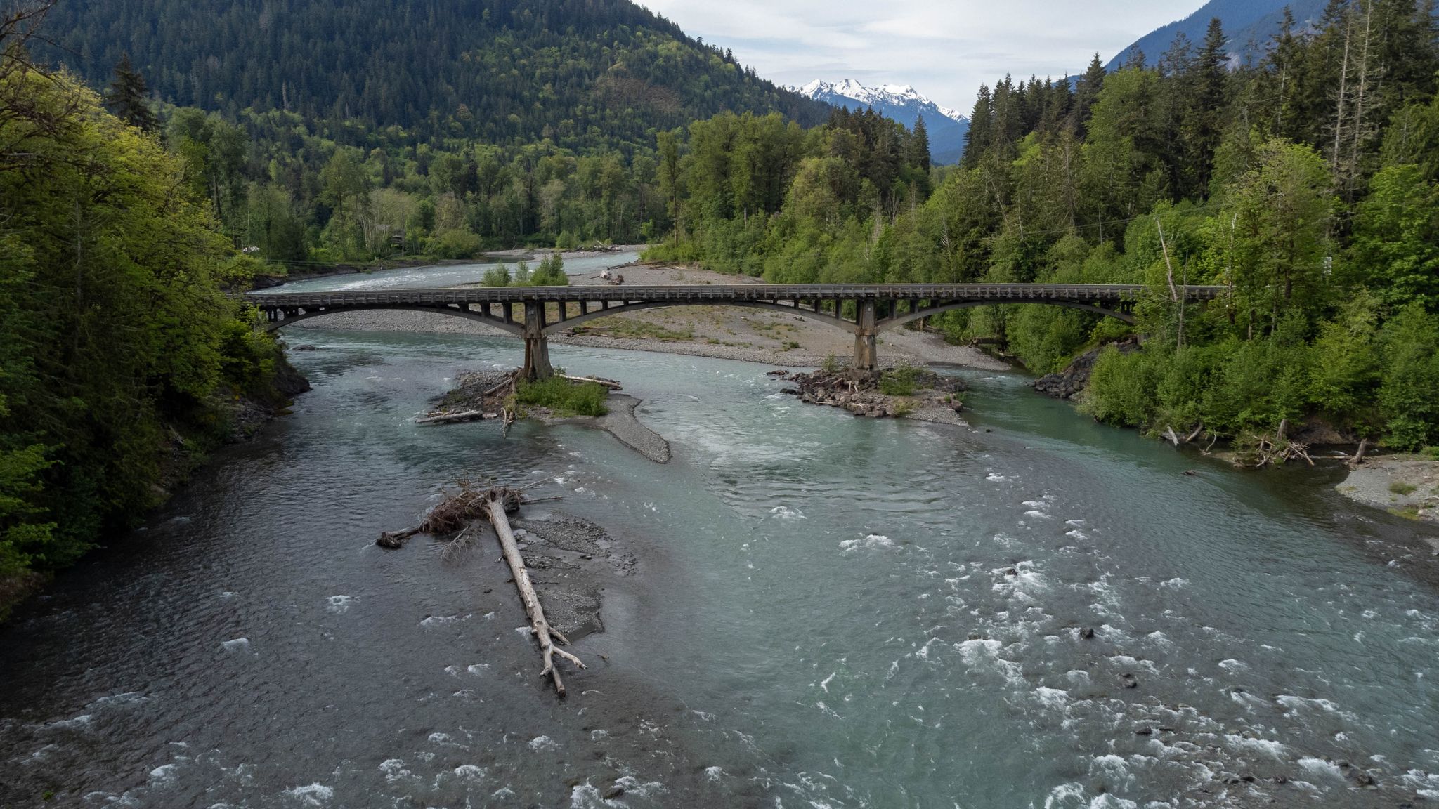 River with a long bridge, surrounded by forested mountains under clouds. - Port Angeles to Lake Crescent loop