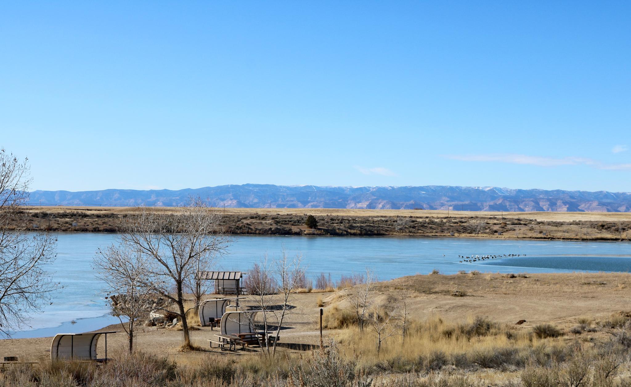 Bright river scene with small shelters on dry banks, distant mountains.
