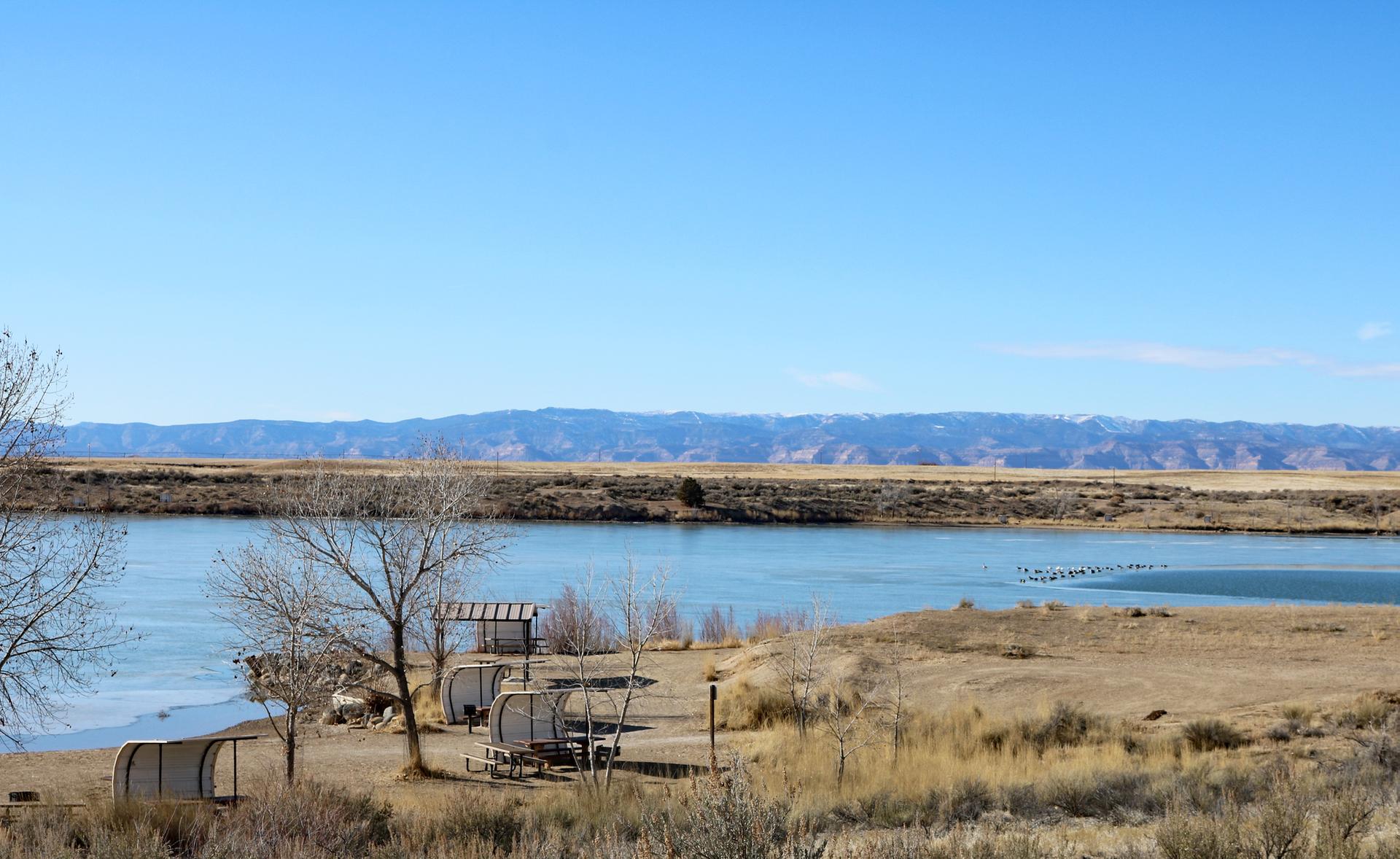 Bright river scene with small shelters on dry banks, distant mountains.