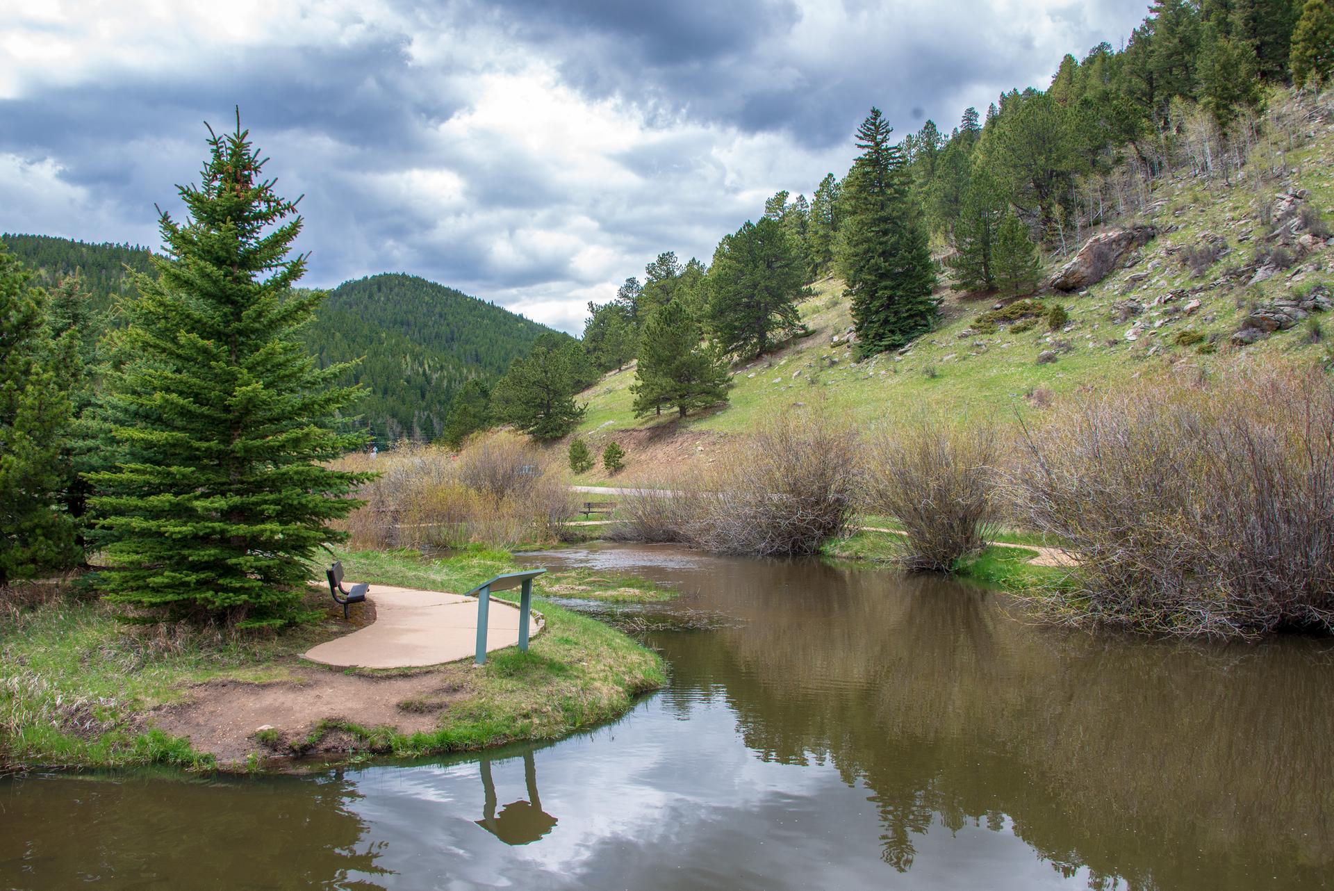 A pond with a wooden viewing platform surrounded by green hills and trees.