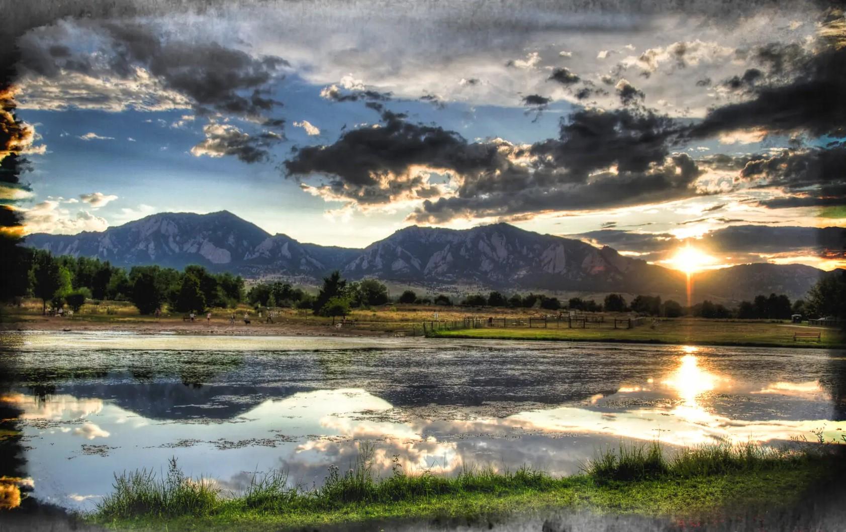 Dramatic sunset over a reflective lake with distant mountains under cloudy skies.