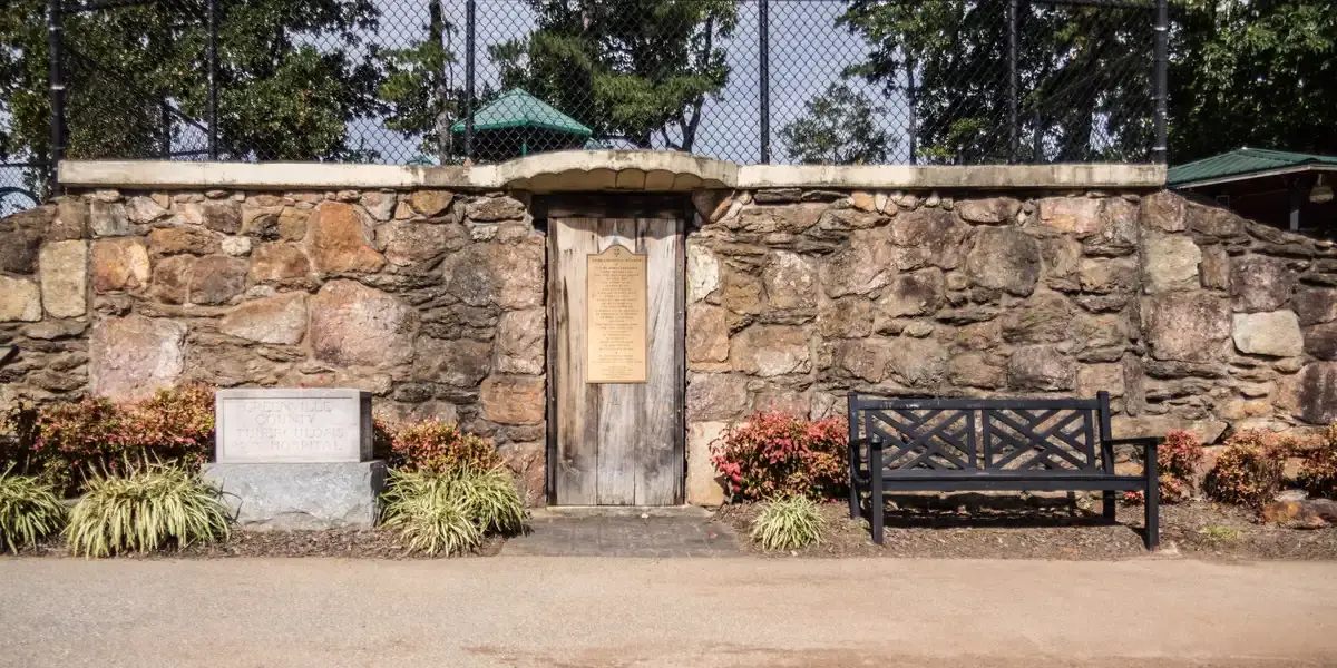 Old stone wall with a wooden door, bench, and plaque under bright light.