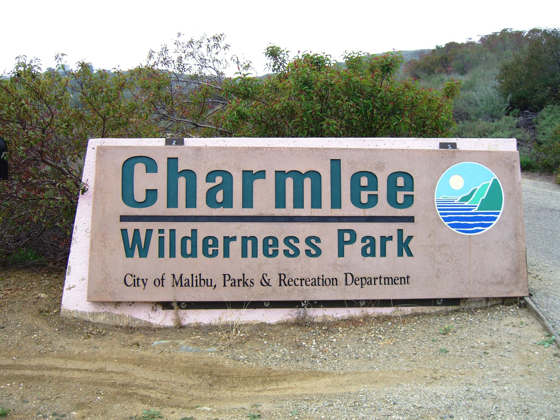 Large park sign on dirt ground with green foliage under bright daylight.