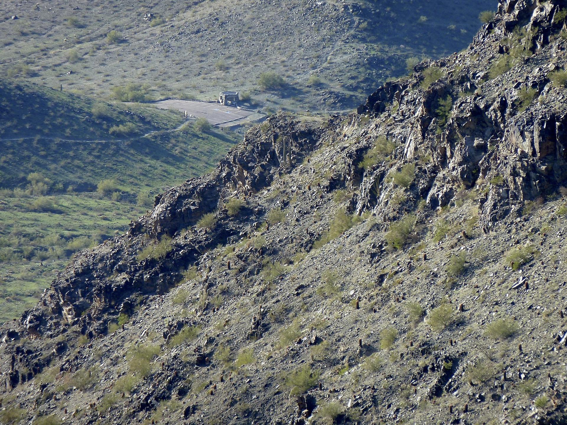 Steep, rocky desert hillside with sparse vegetation and a distant road.