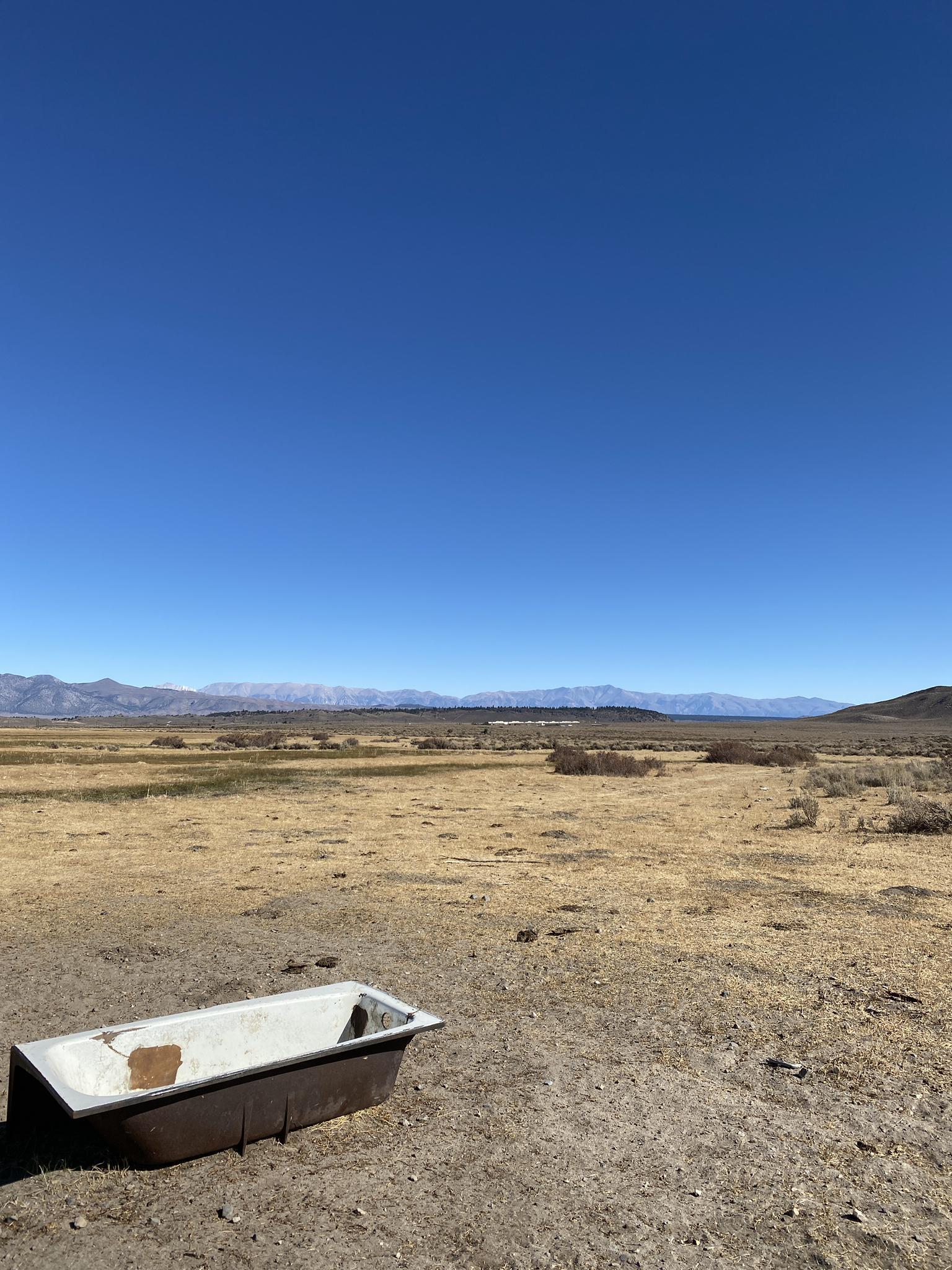 An old bathtub sits in a vast, dry, open landscape under a clear sky.
