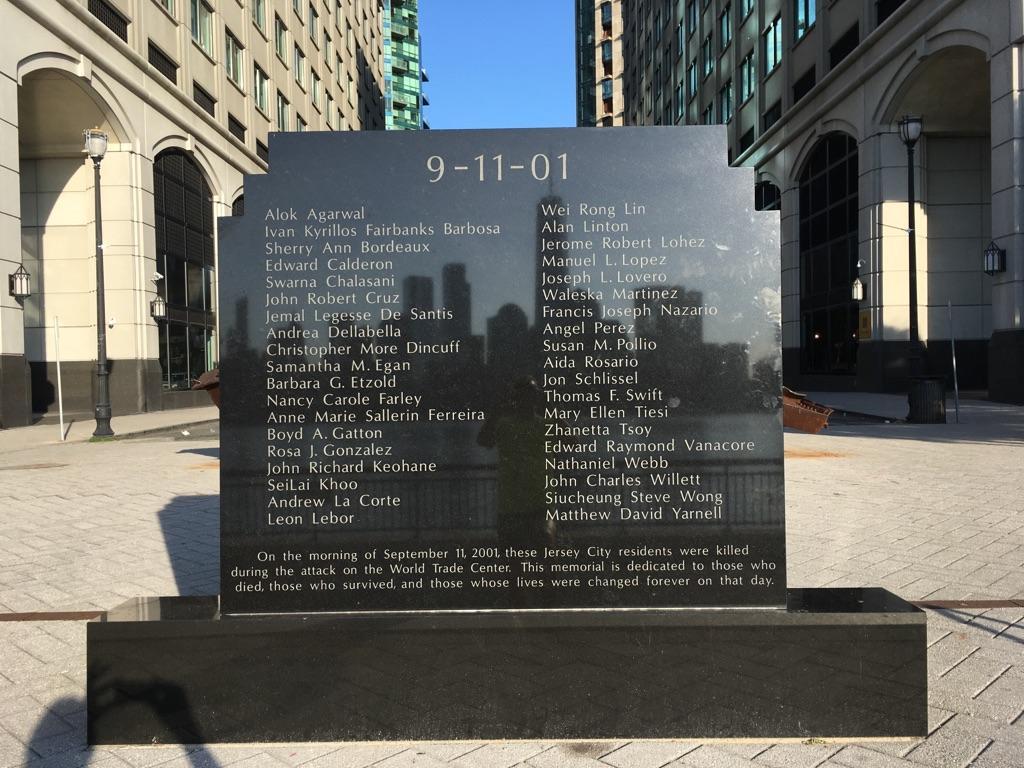 Dark stone memorial plaque with names, surrounded by urban buildings.