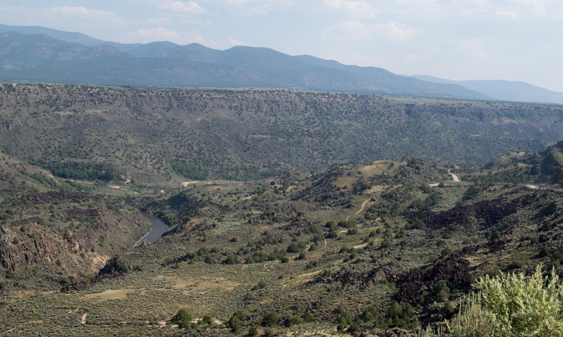 Panoramic view of a deep, winding canyon with a river and distant mountains.