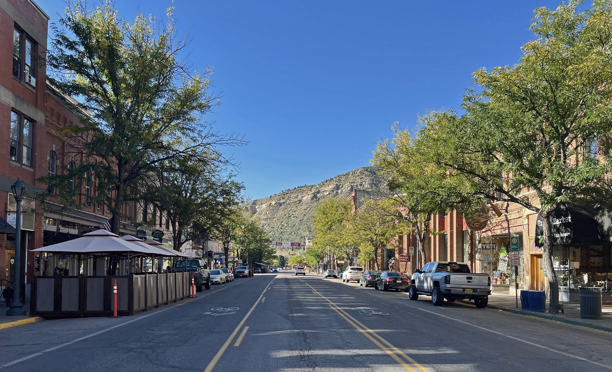 A wide street lined with buildings and trees, leading towards distant mountains. - Smelter Mountain loop