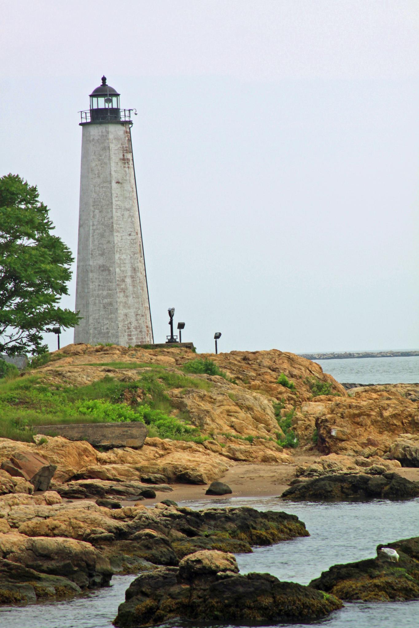 Tall white lighthouse on a rocky, grassy coast under an overcast sky.
