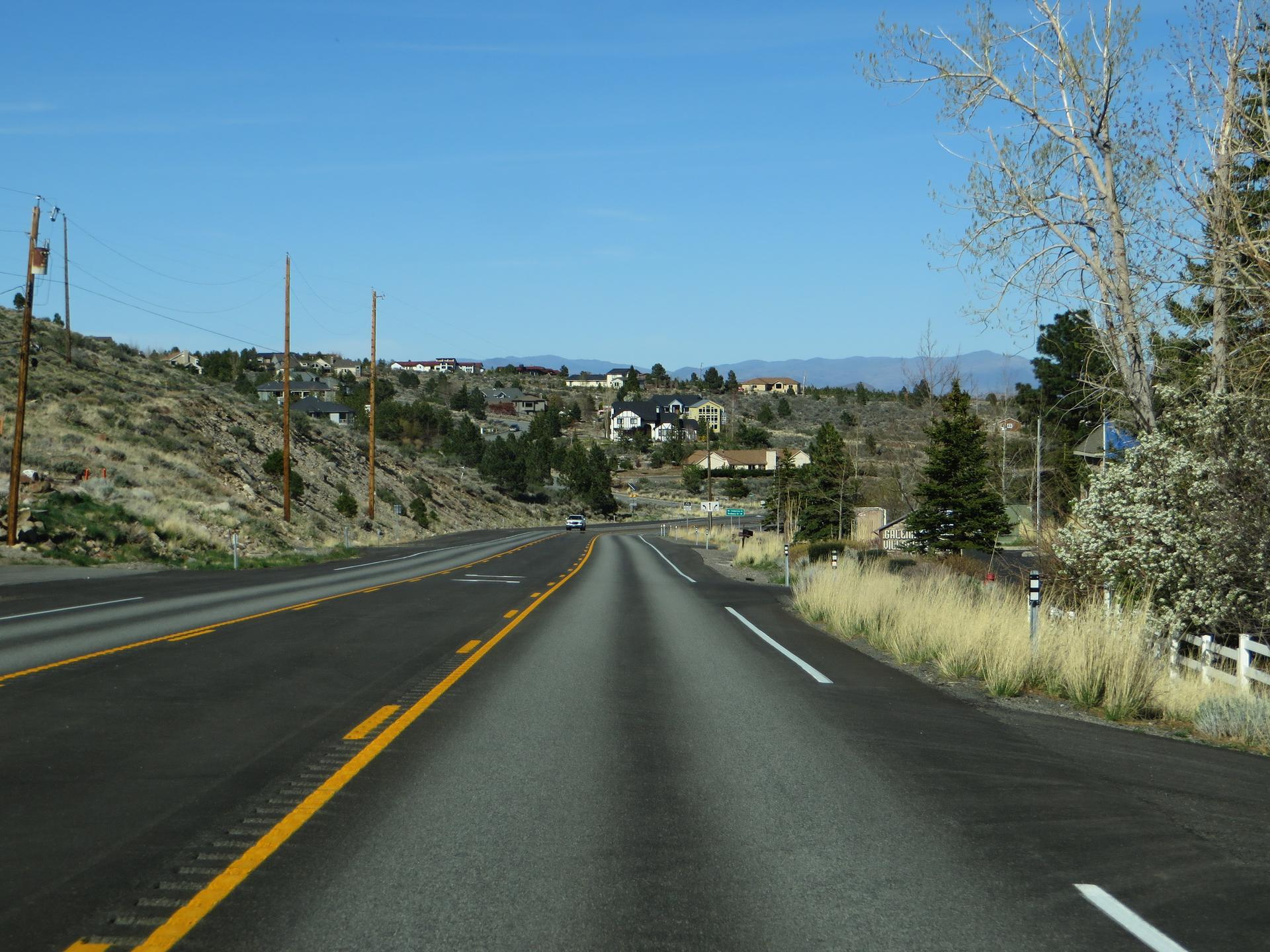 Paved road winding through hills with distant houses under a clear sky.