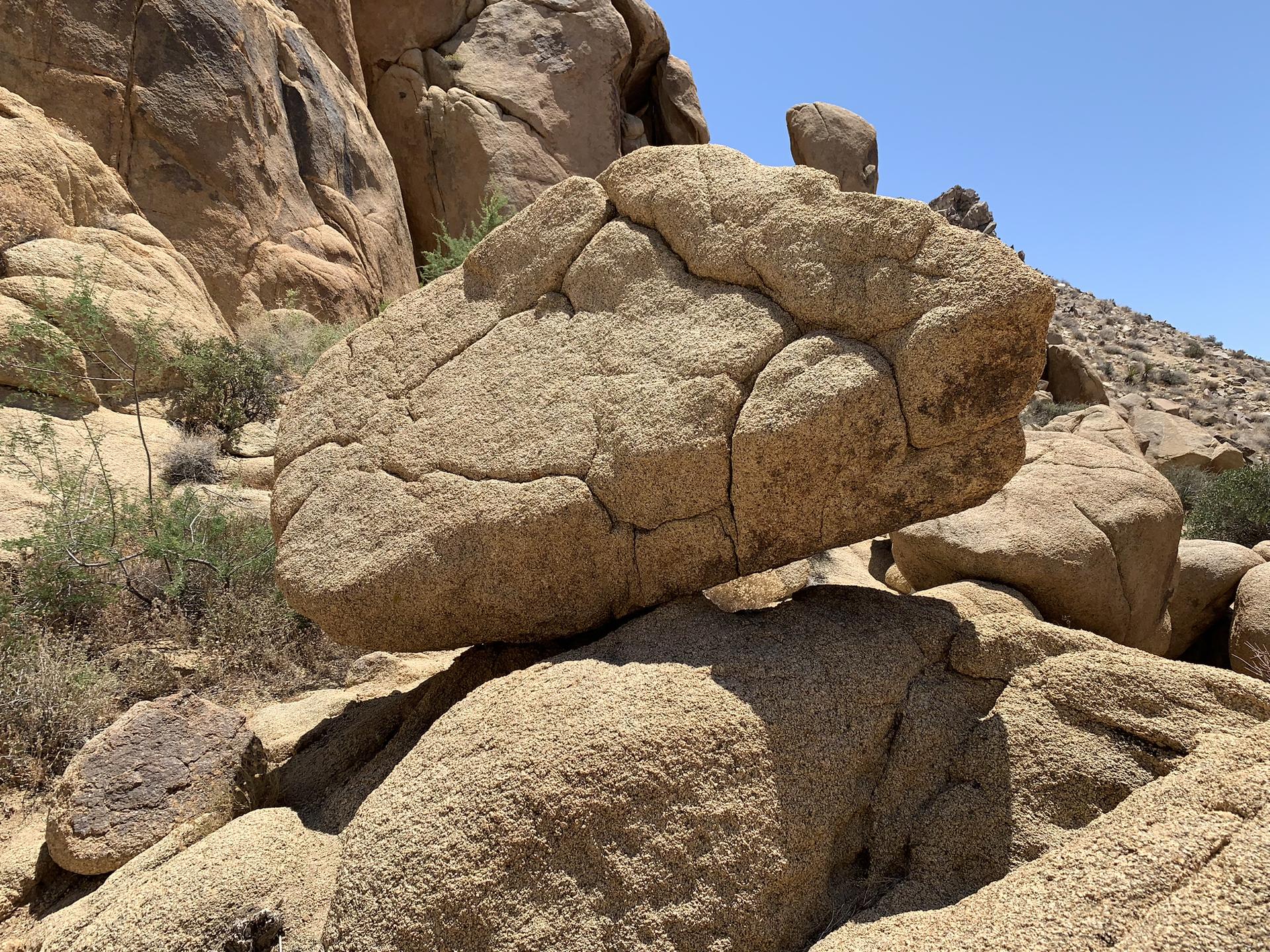 A large, textured boulder balanced on smaller rocks in a sunny desert.