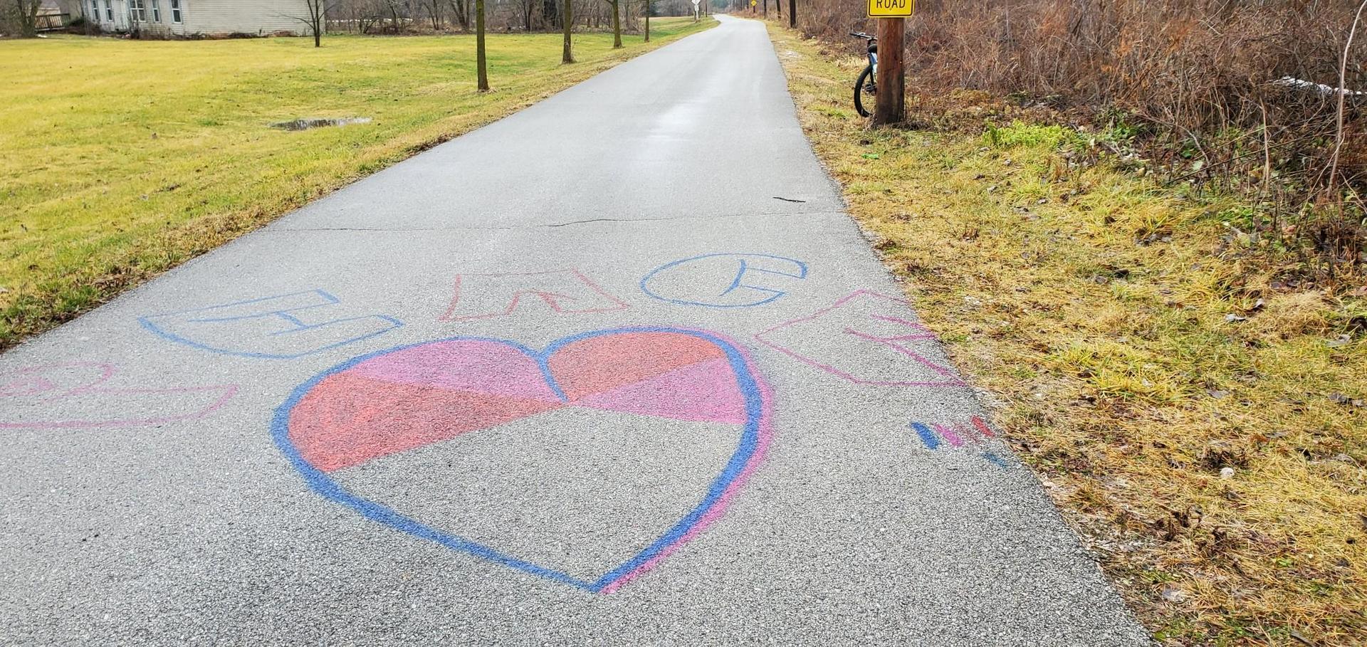 Chalk heart and text on a paved path with grassy edges under soft light.