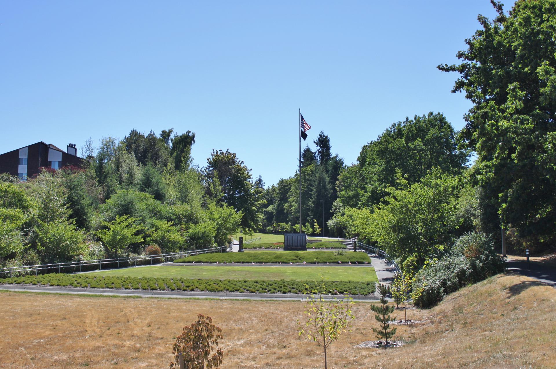 Sunny park with green lawns, trees, a flagpole, and a monument.