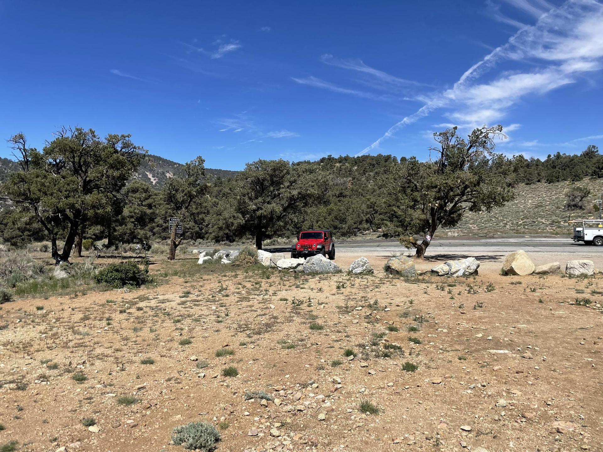 Red jeep parked on a dirt lot near a road, sunny day.