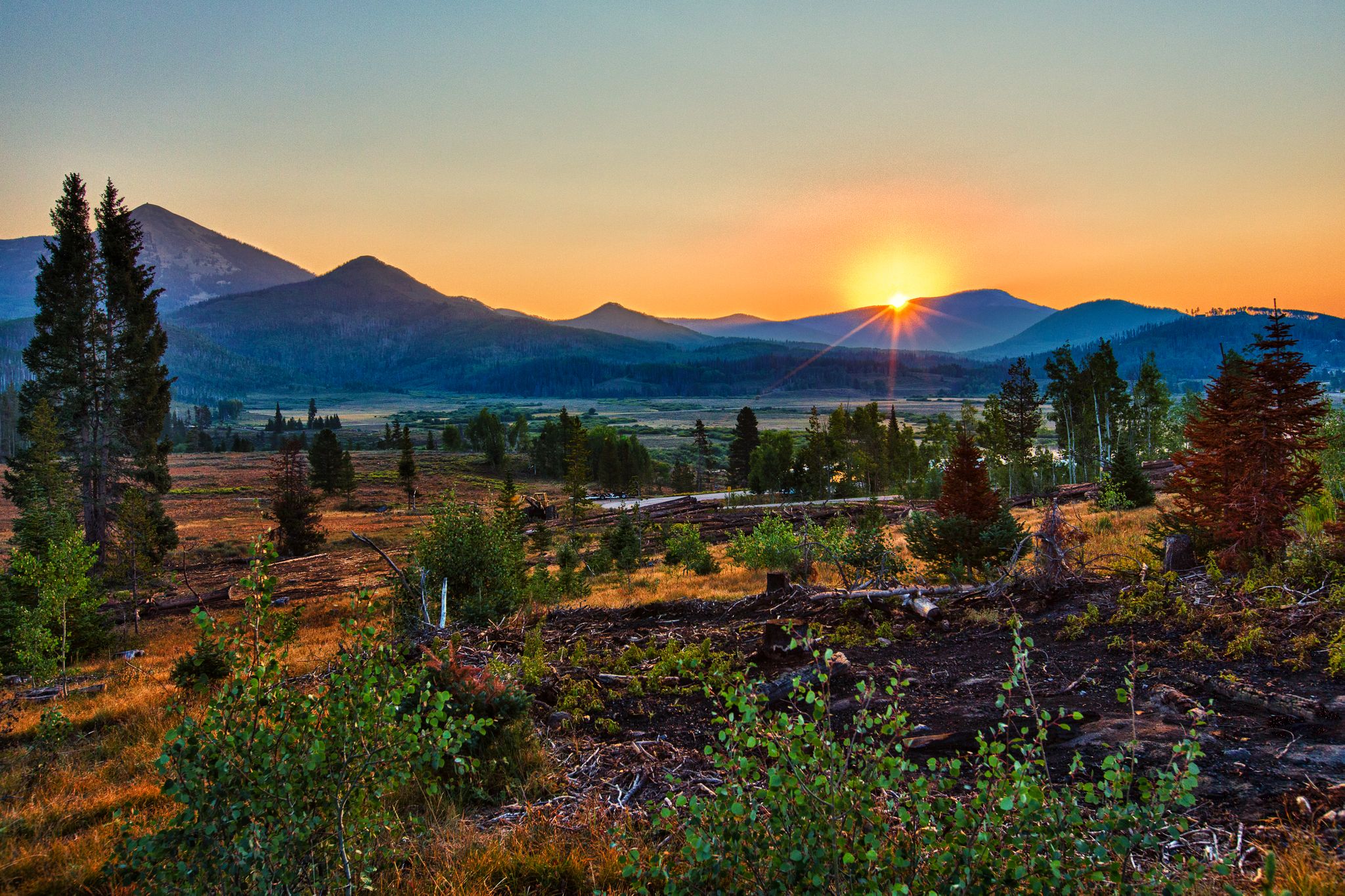 Golden sunset over a mountain range with a forested valley below. - Willow Creek Trail