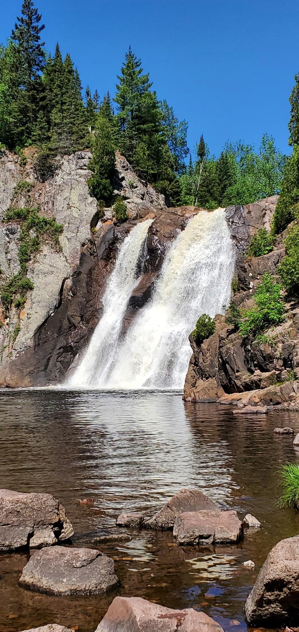 Powerful waterfall cascading into a rocky river, surrounded by green trees.