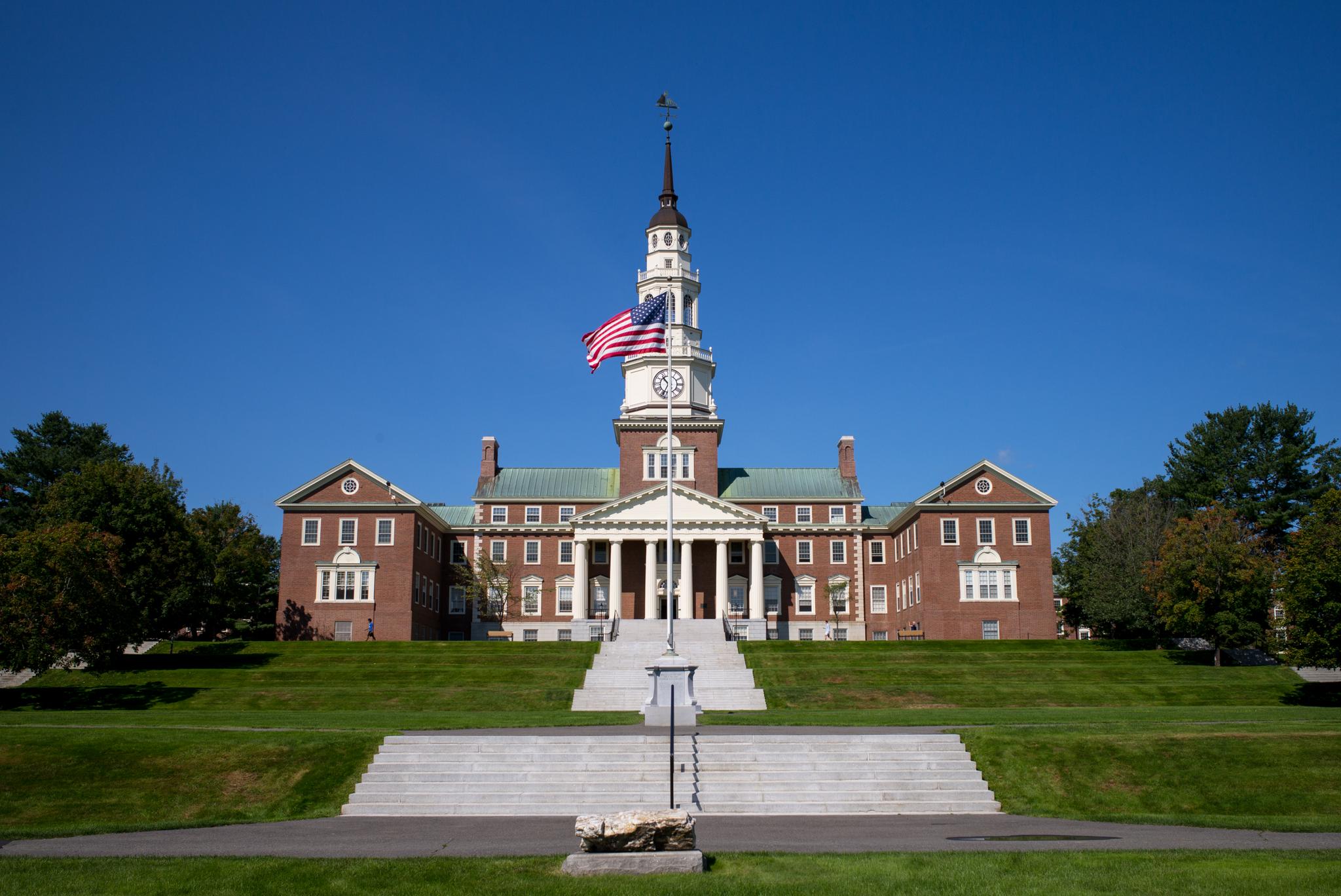 Grand brick building with a clock tower and flag on a sunny day.