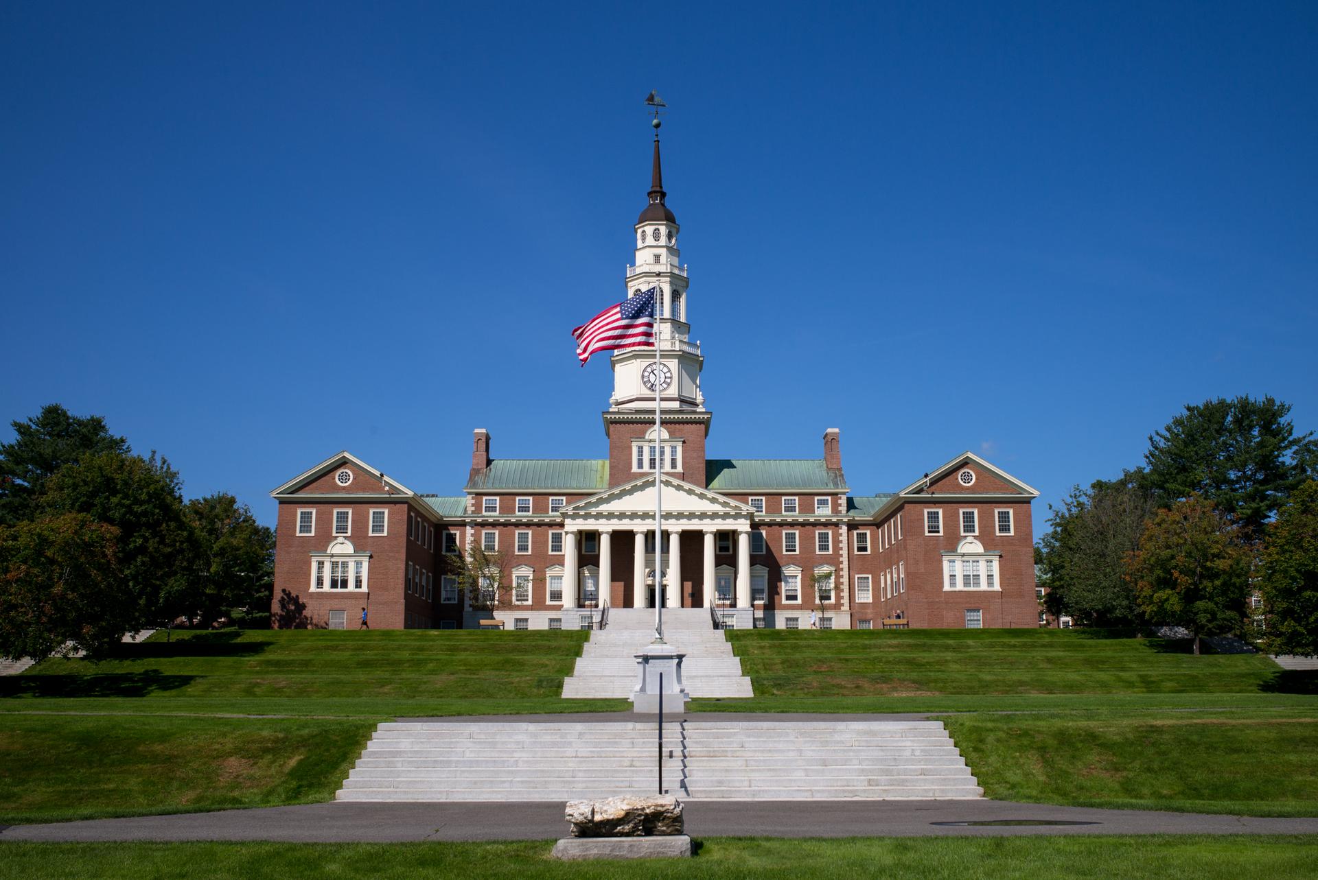 Grand brick building with a clock tower and flag on a sunny day.