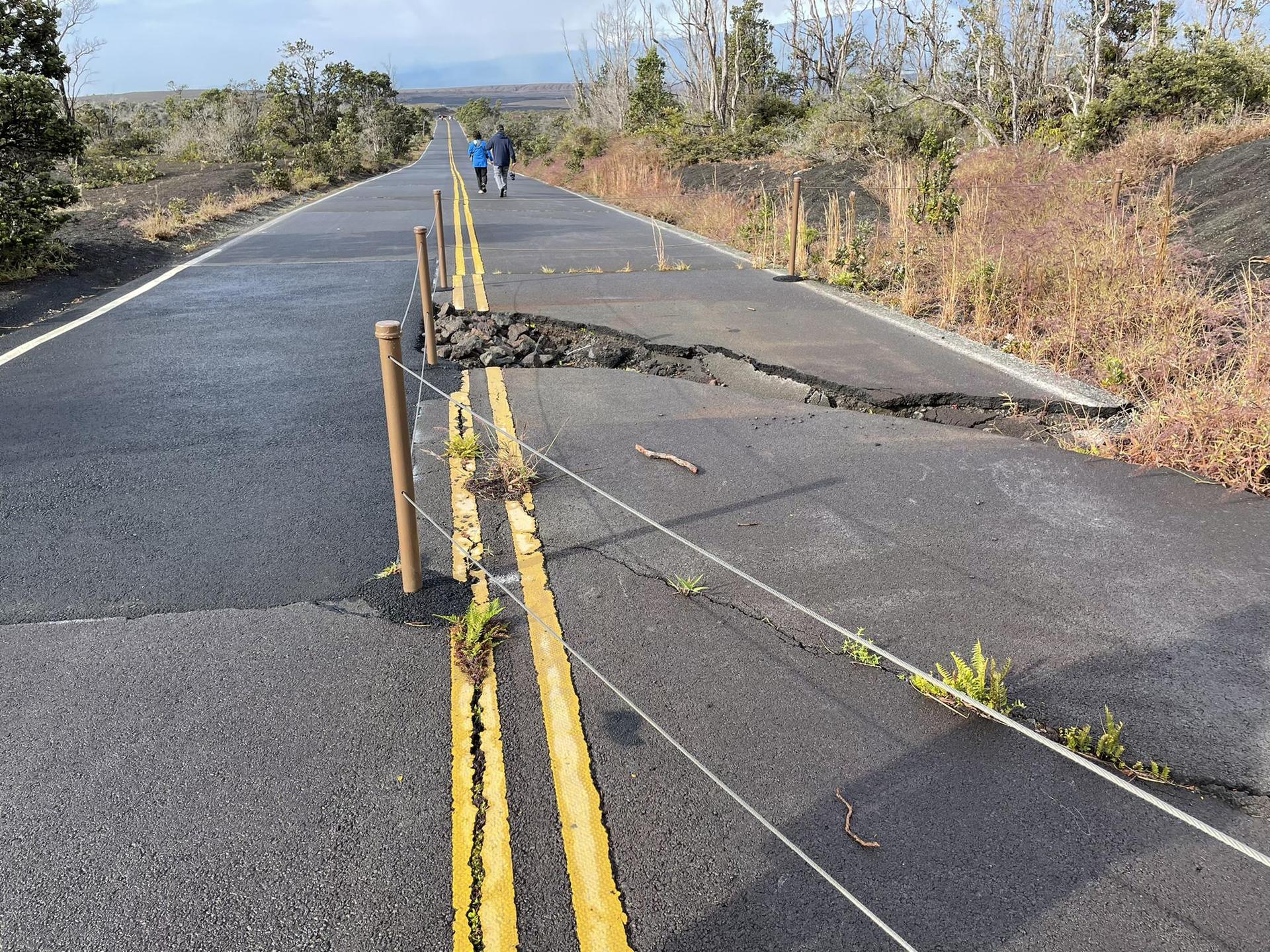A cracked road with a large fissure, two people walk in the distance.