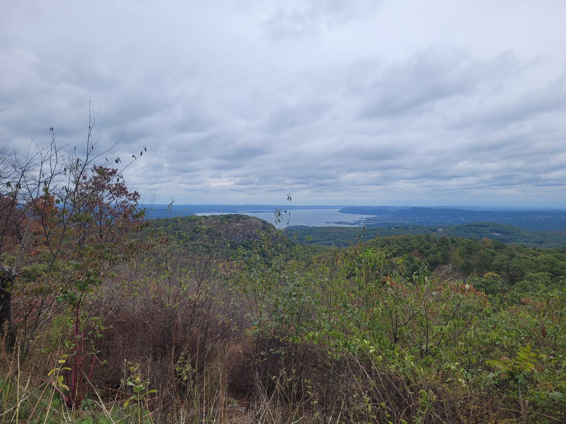 Overcast view of forested hills and a large body of water in the distance.