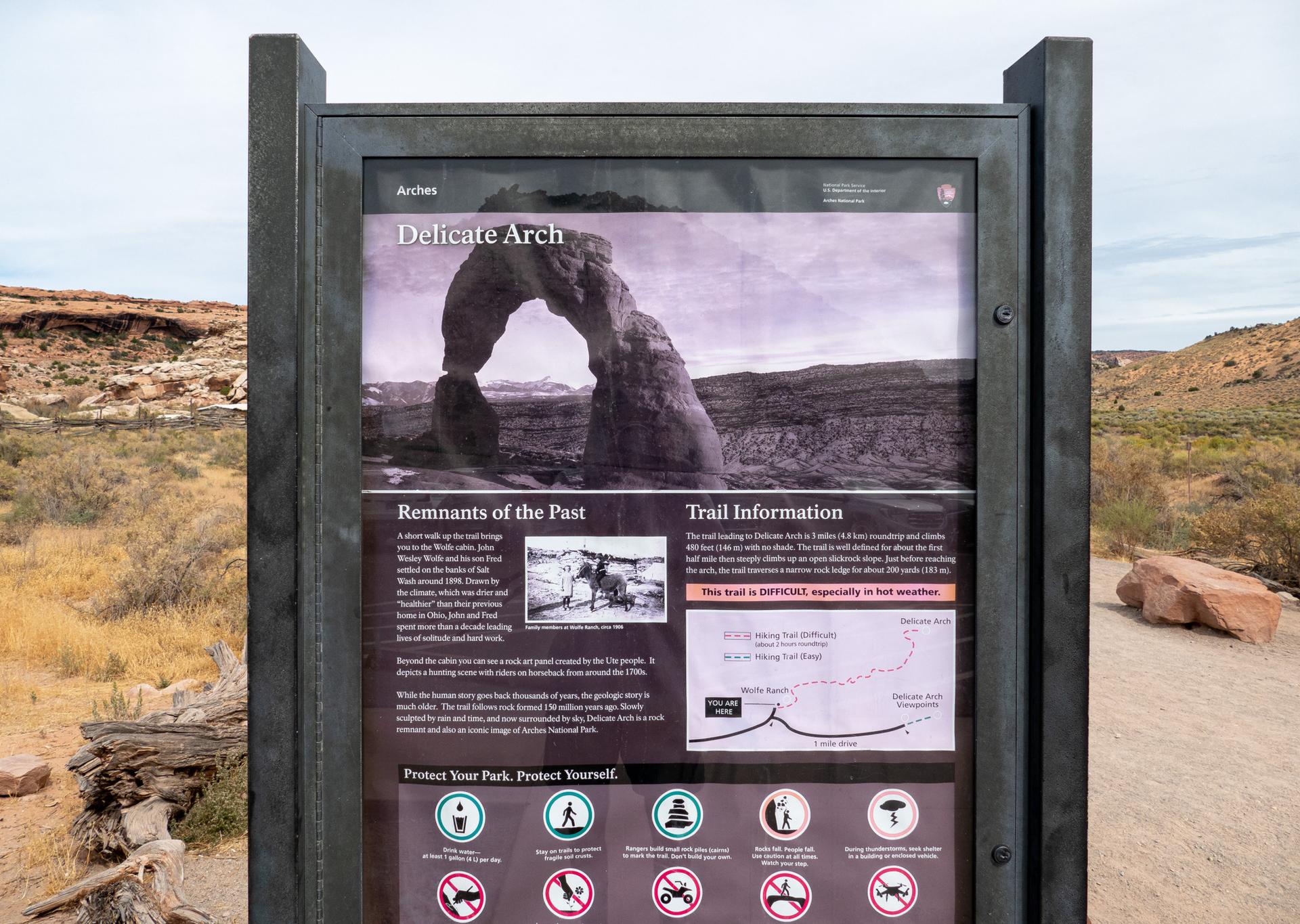A trail information sign with images and text in a desert environment.