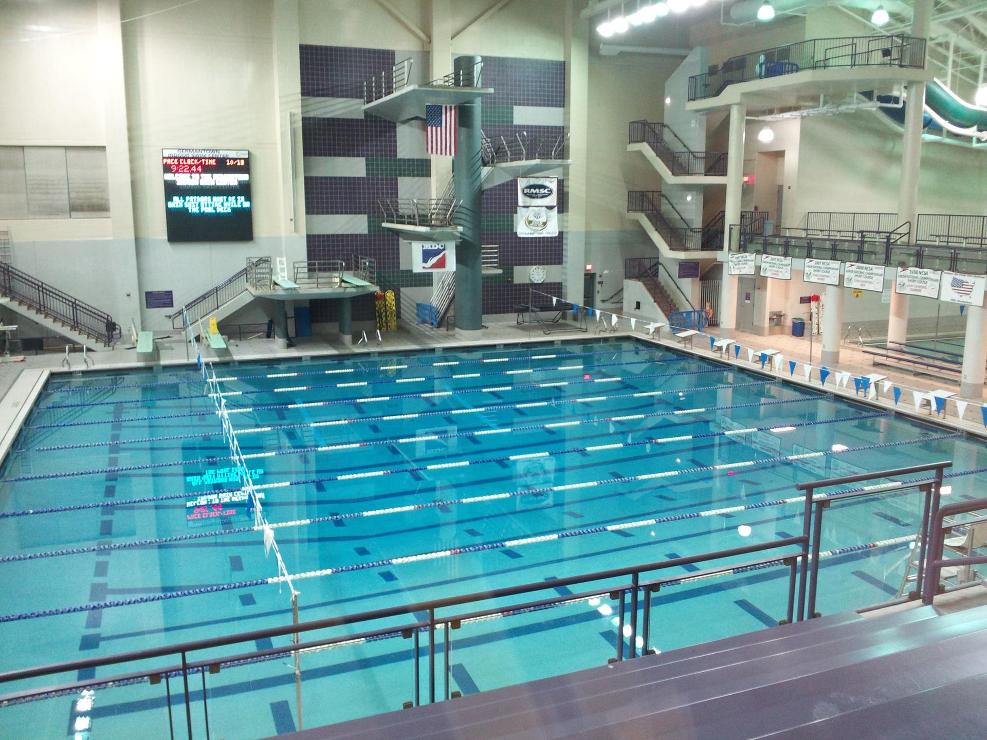 Large indoor swimming pool with multiple diving platforms under bright lights.
