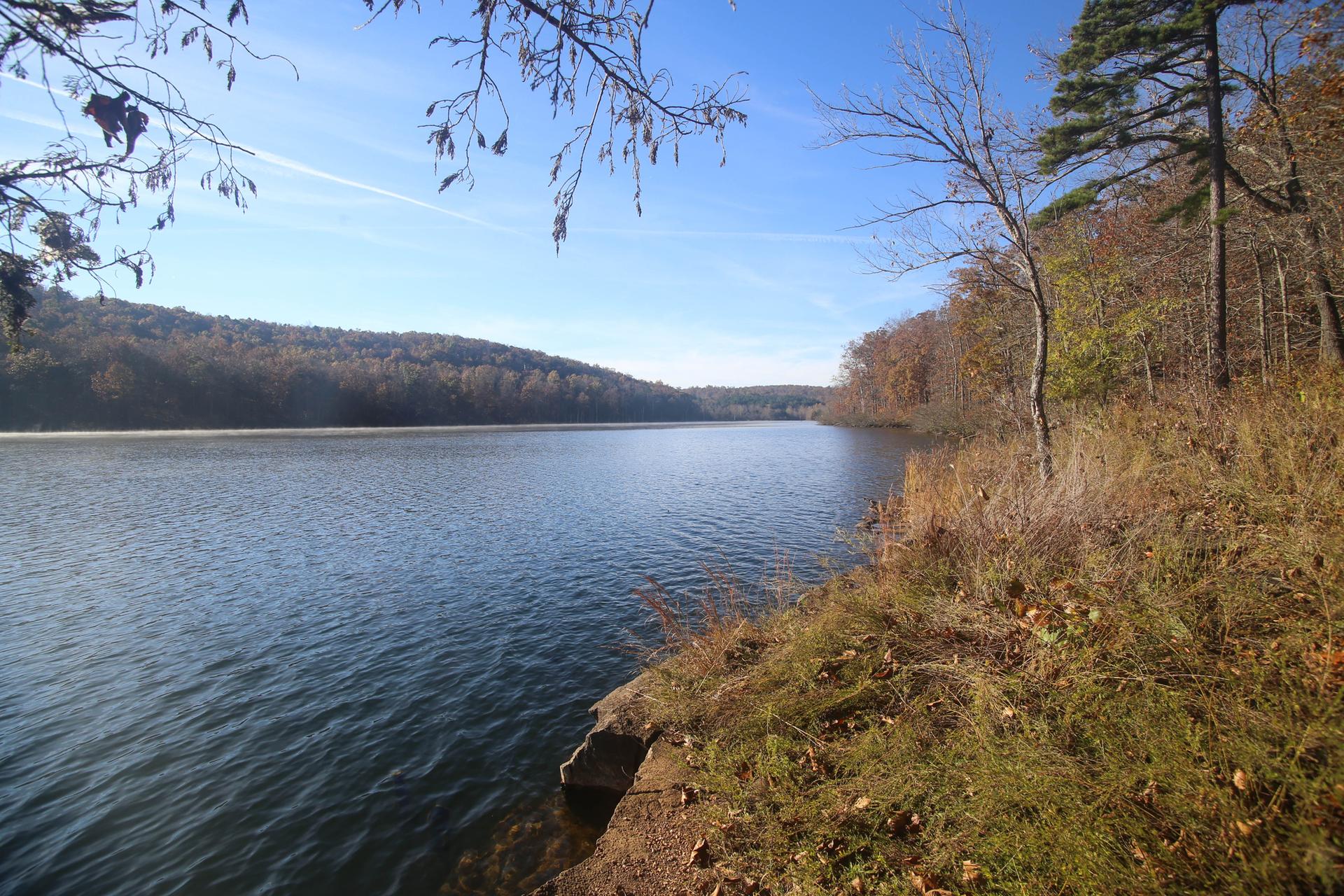 A wide lake surrounded by autumn trees under a clear blue sky.