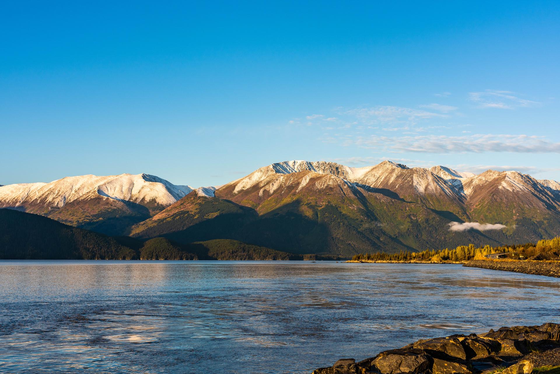 Calm water reflecting snow-capped mountains under a clear blue sky.
