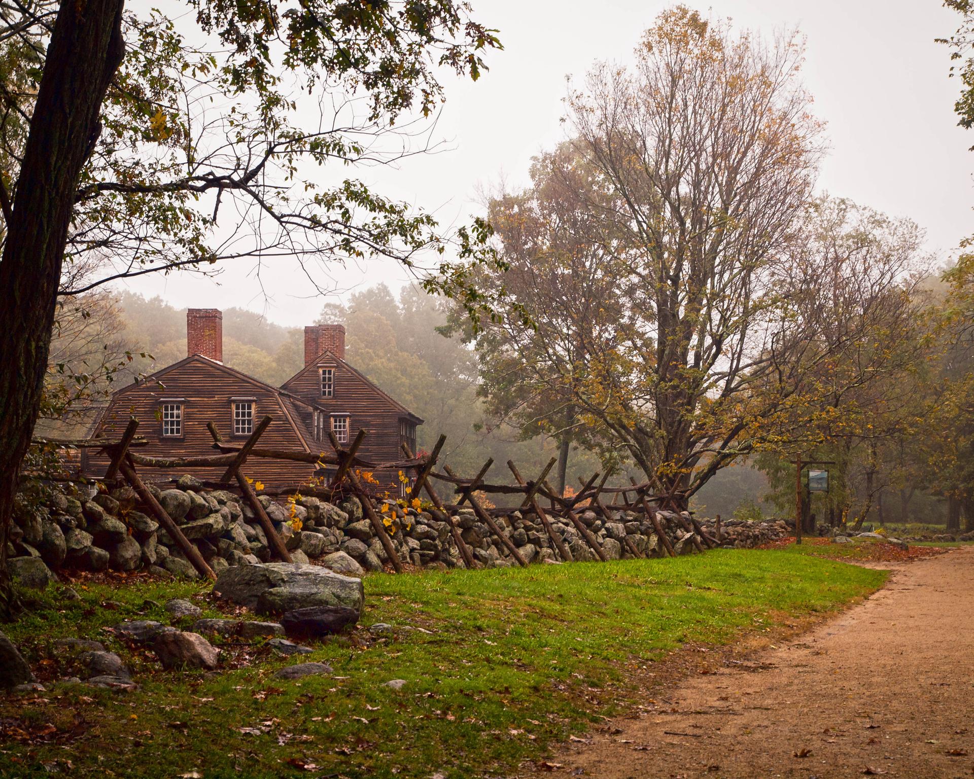 Old wooden houses behind a rustic fence on a misty autumn day.