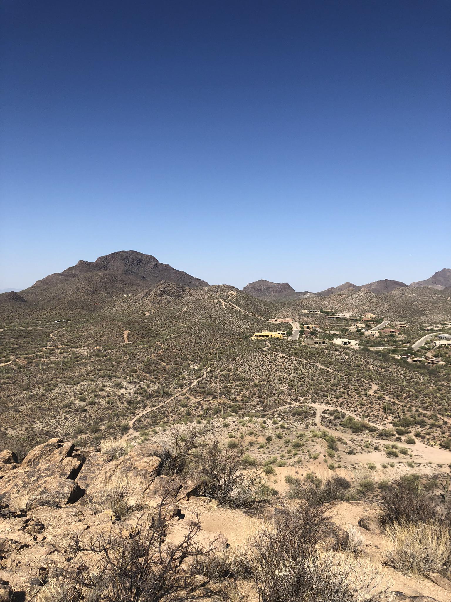 Vast desert landscape with mountains, sparse brush, and distant homes under clear sky.